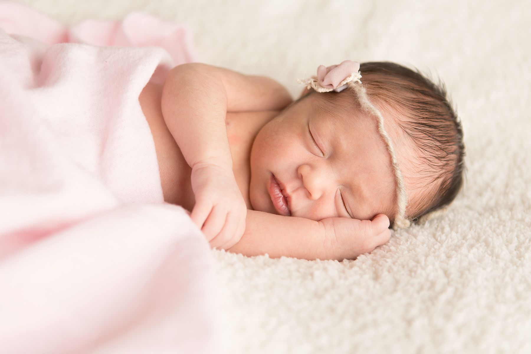 Peaceful newborn baby sleeping on soft white blanket with pink accents.