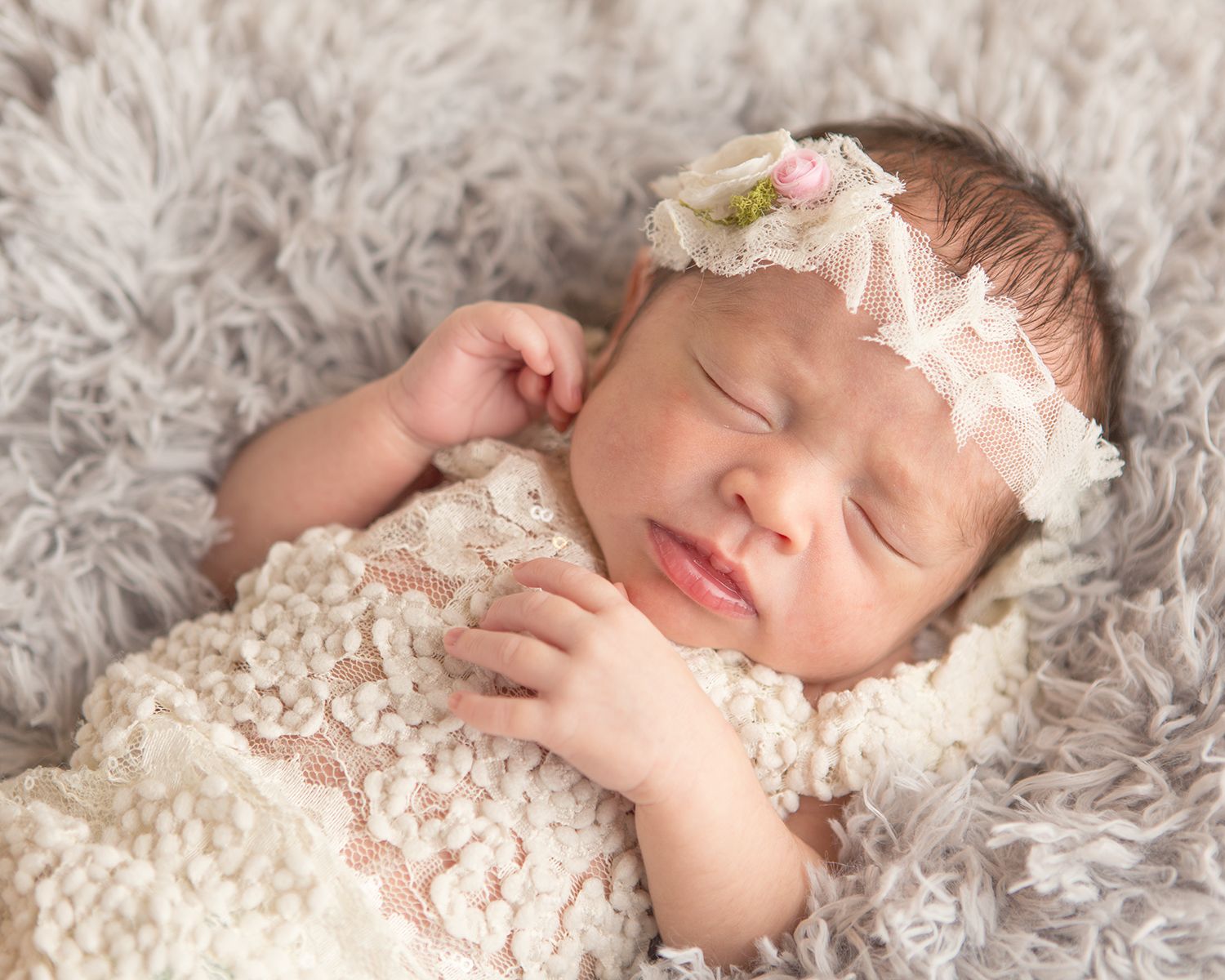 Sweet newborn portrait on cream textured blanket with lace accessories.
