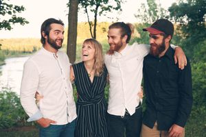 A group of four people sharing a warm moment together outdoors near a river at sunset.