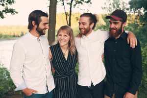 Four people pose together outdoors wearing casual attire against a natural backdrop.