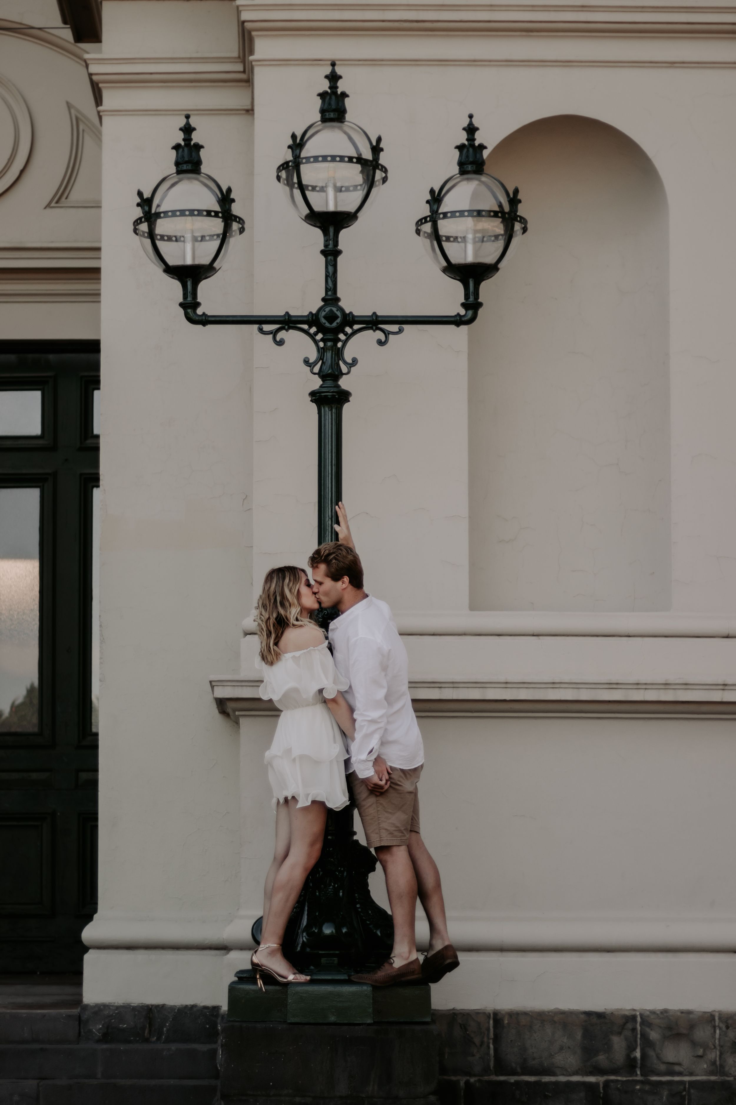 A couple kissing while leaning on a lamp post.