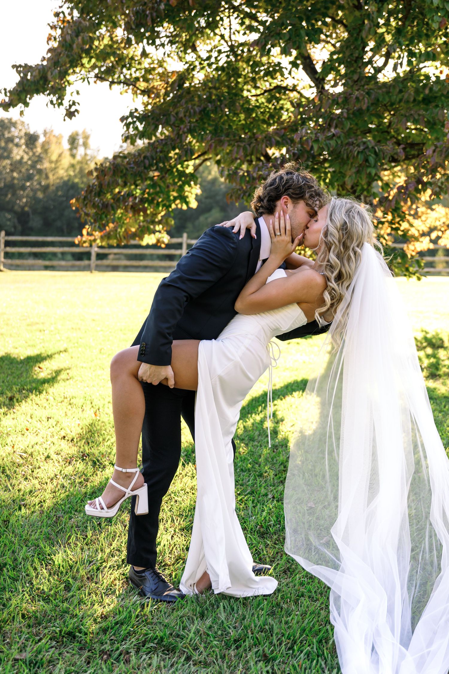 A romantic photoshoot in a sunlit field with flowing white dress and dramatic dip poses.
