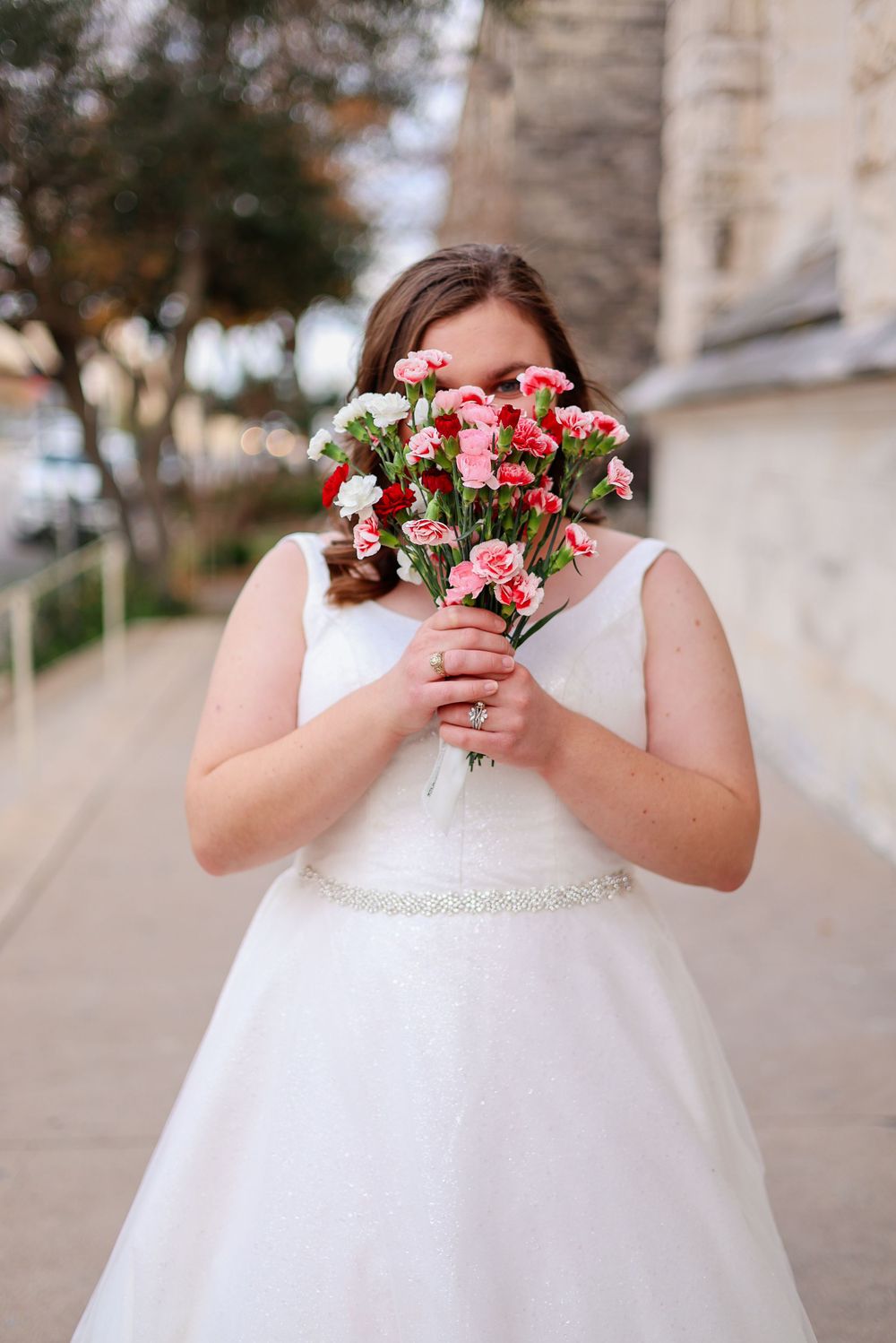 Bride in white dress holding pink and white flower bouquet.