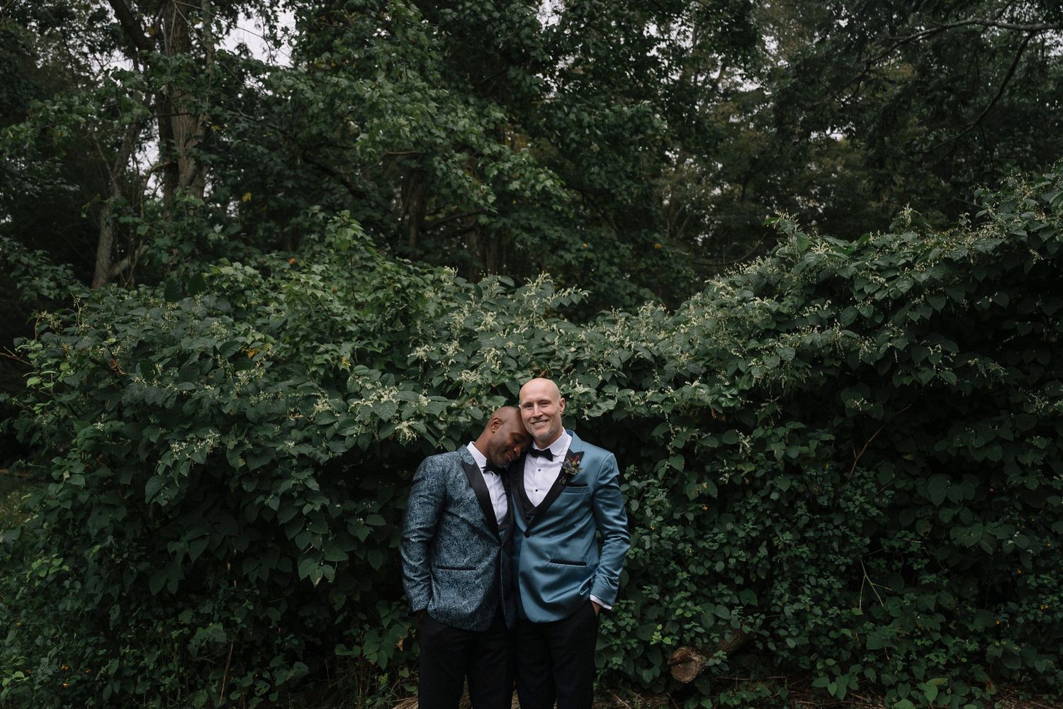Romantic portrait of couple in blue suits against lush garden backdrop.