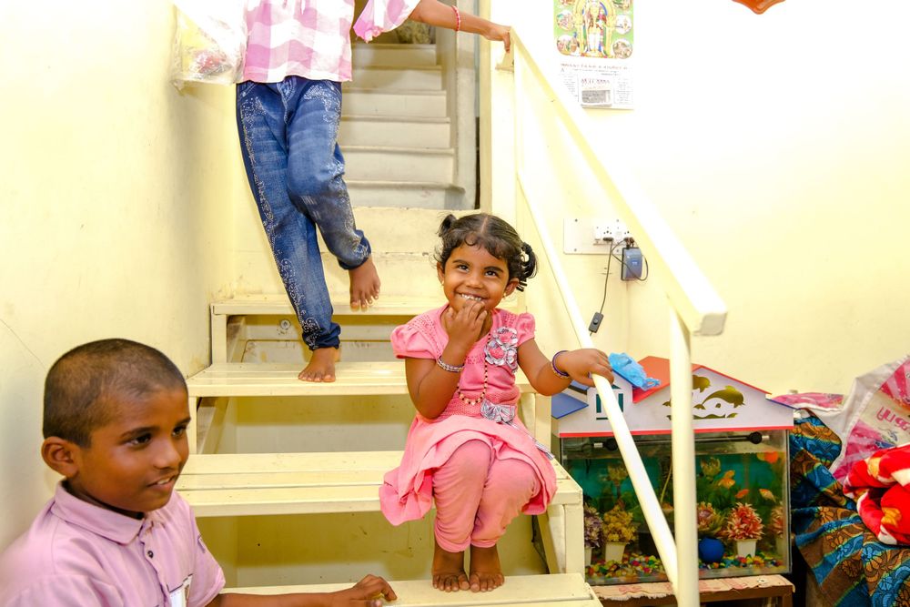 Children sitting on indoor stairs with toys and casual clothing in a home setting.