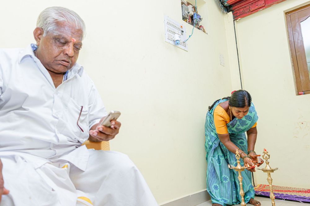 Two people perform traditional rituals in a corner room with white walls during a ceremony.