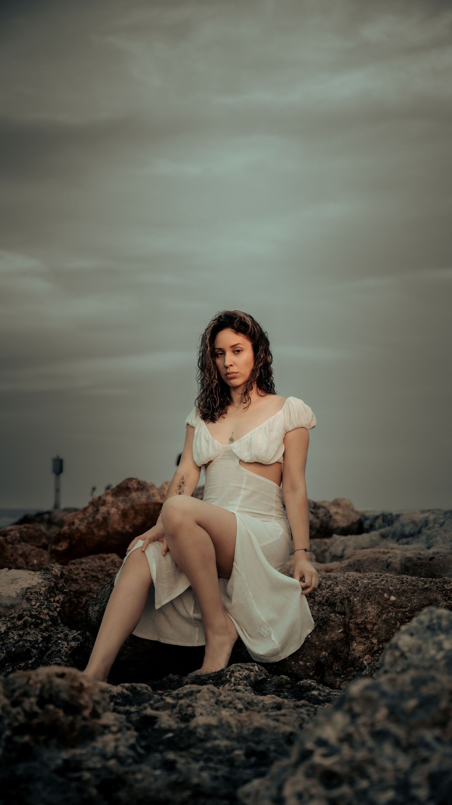 Atmospheric portrait on rocky coastline with dramatic cloudy sky backdrop.