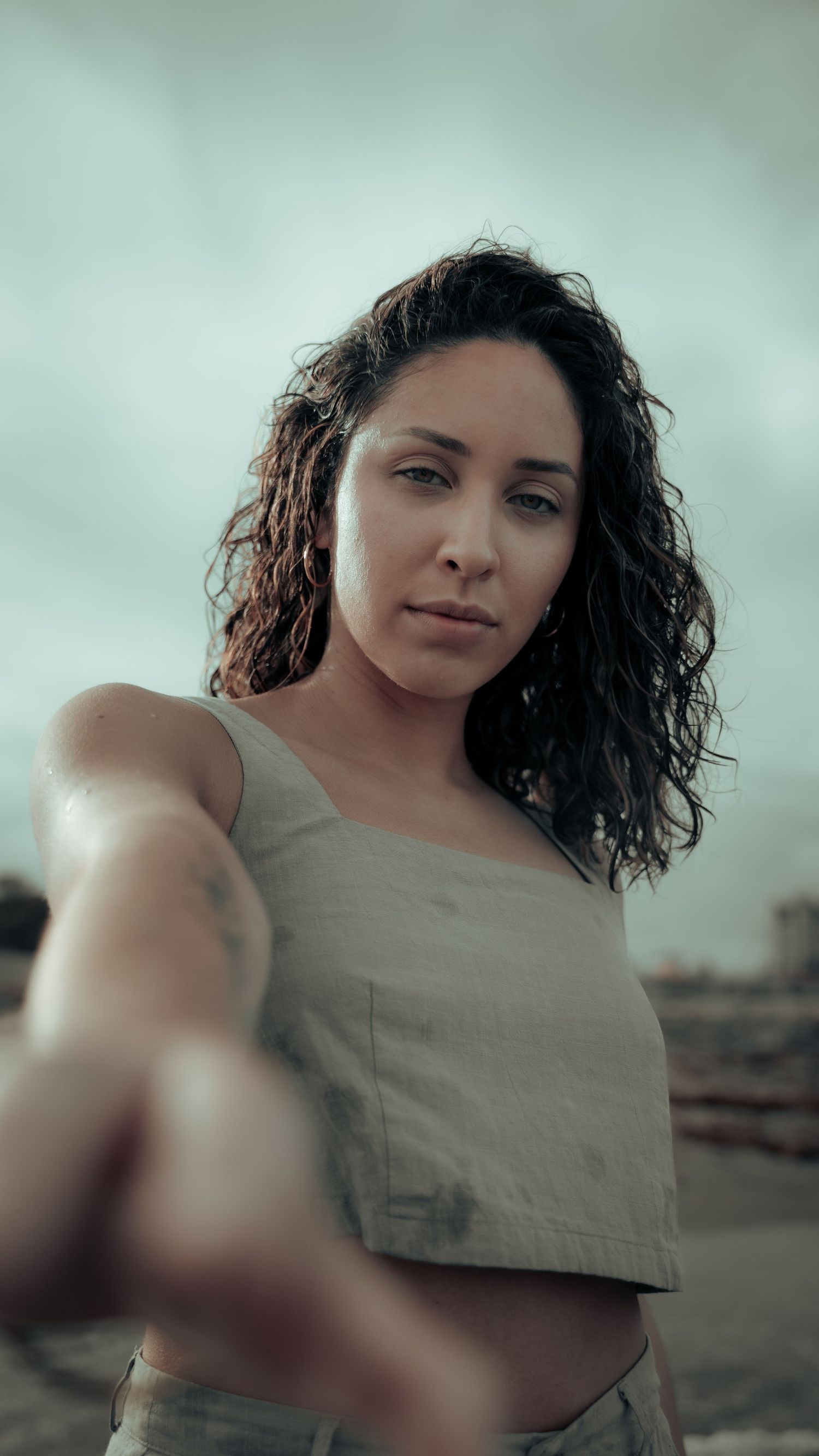 A selfie perspective of someone with curly hair wearing a crop top against an overcast sky.