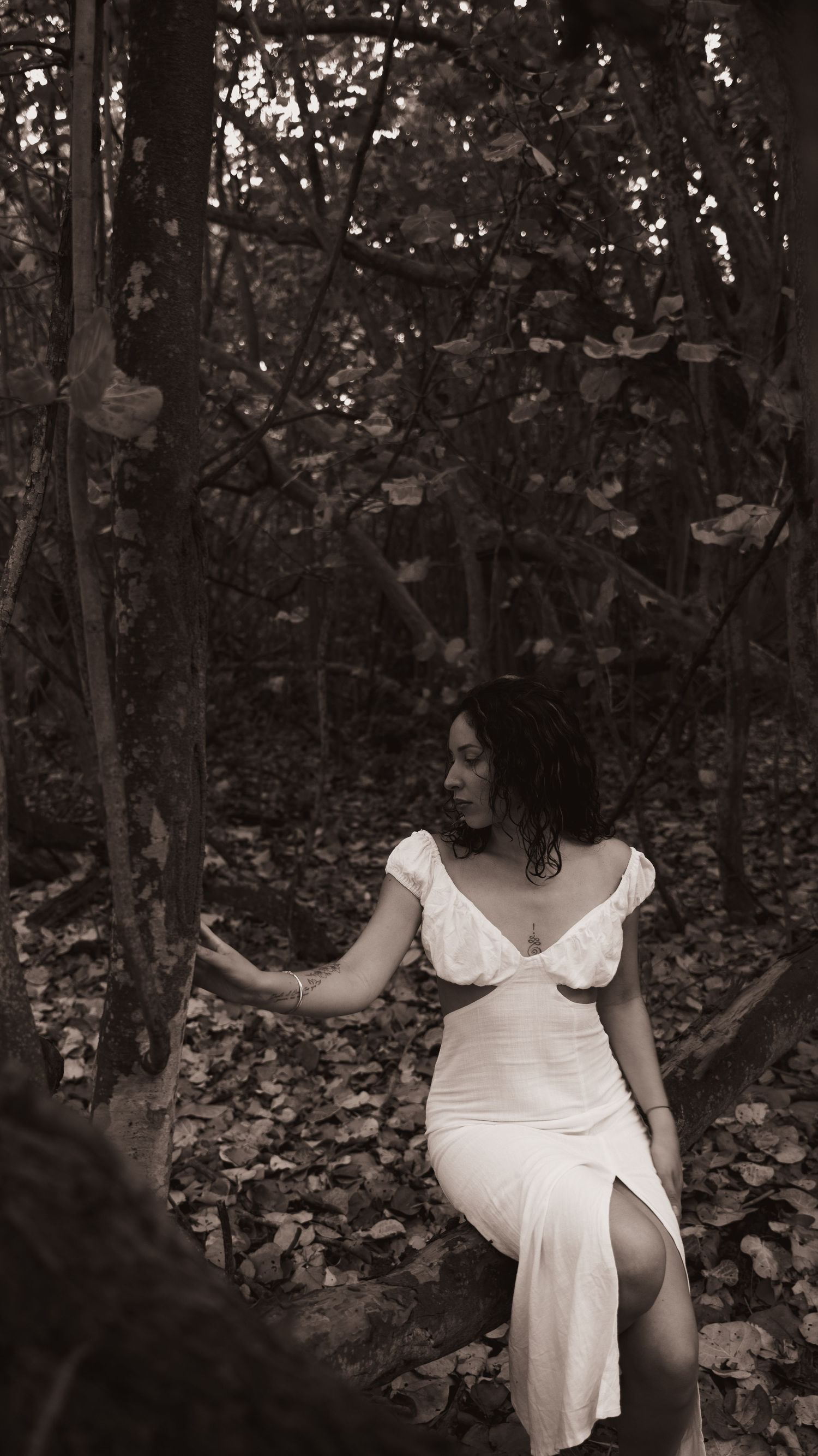 A vintage-style portrait in a flowing white dress amid a forest setting.