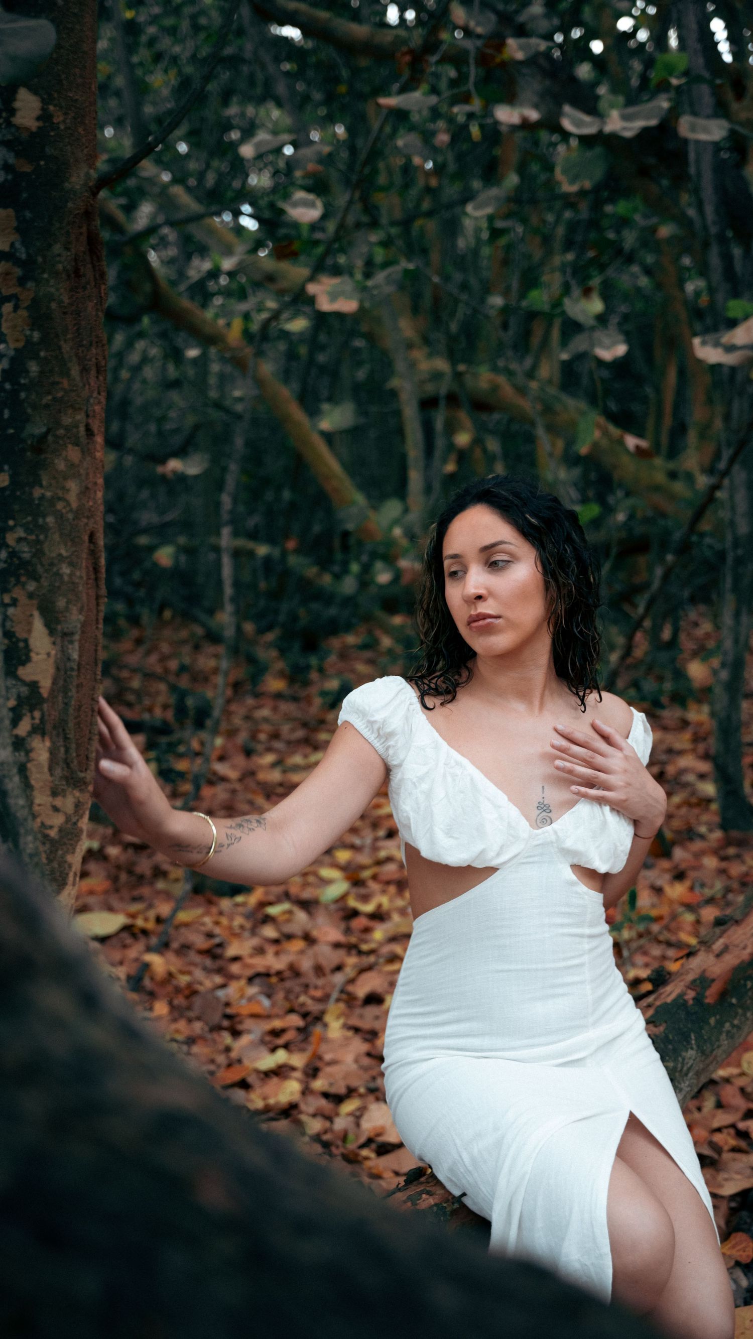 An artistic portrait in a white dress against a moody forest backdrop.
