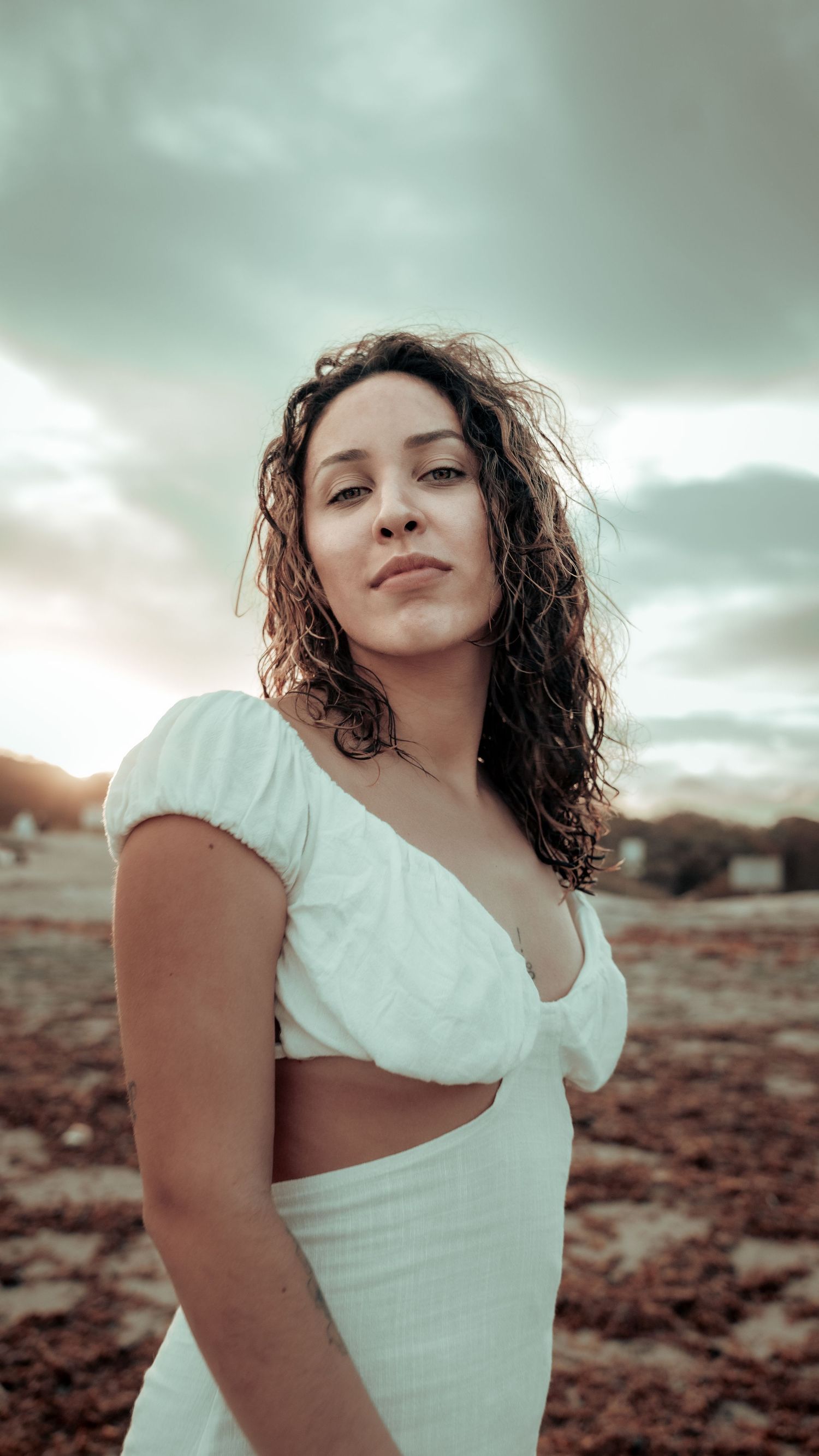 Dramatic portrait against cloudy sky wearing a white dress in desert terrain.