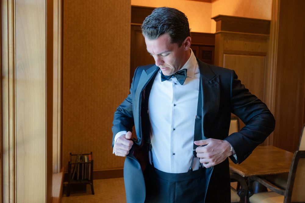 Person adjusting black tuxedo jacket and bowtie while getting dressed.