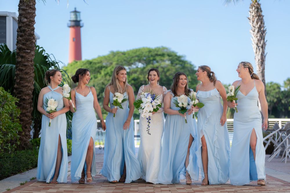 Bridesmaids in light blue dresses standing together near a red lighthouse.