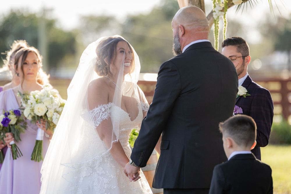 Wedding ceremony takes place outdoors during golden hour with floral bouquets and veil flowing in afternoon light.