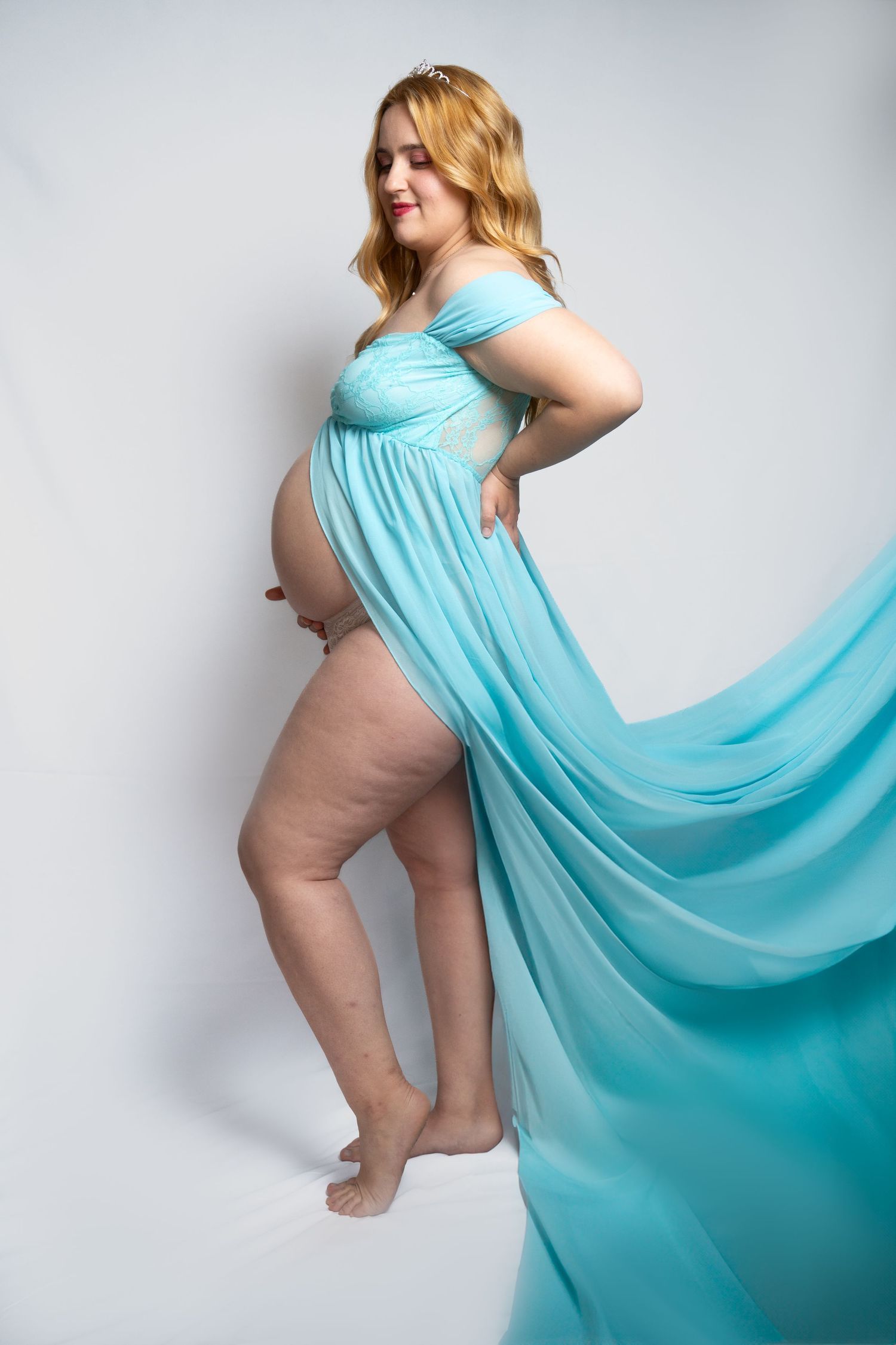 Woman in flowing turquoise fabric poses elegantly against white background.