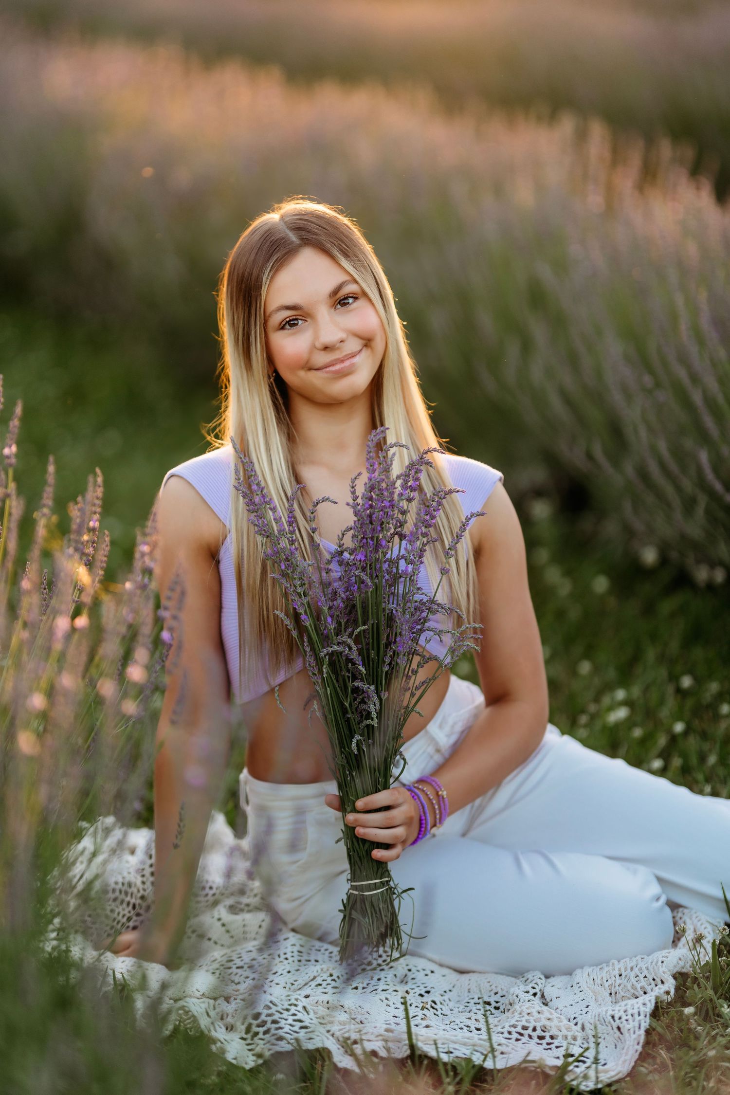 A person in a white dress sits among blooming purple lavender flowers at sunset in a dreamy summer field..  Middle TN Tween Photographer