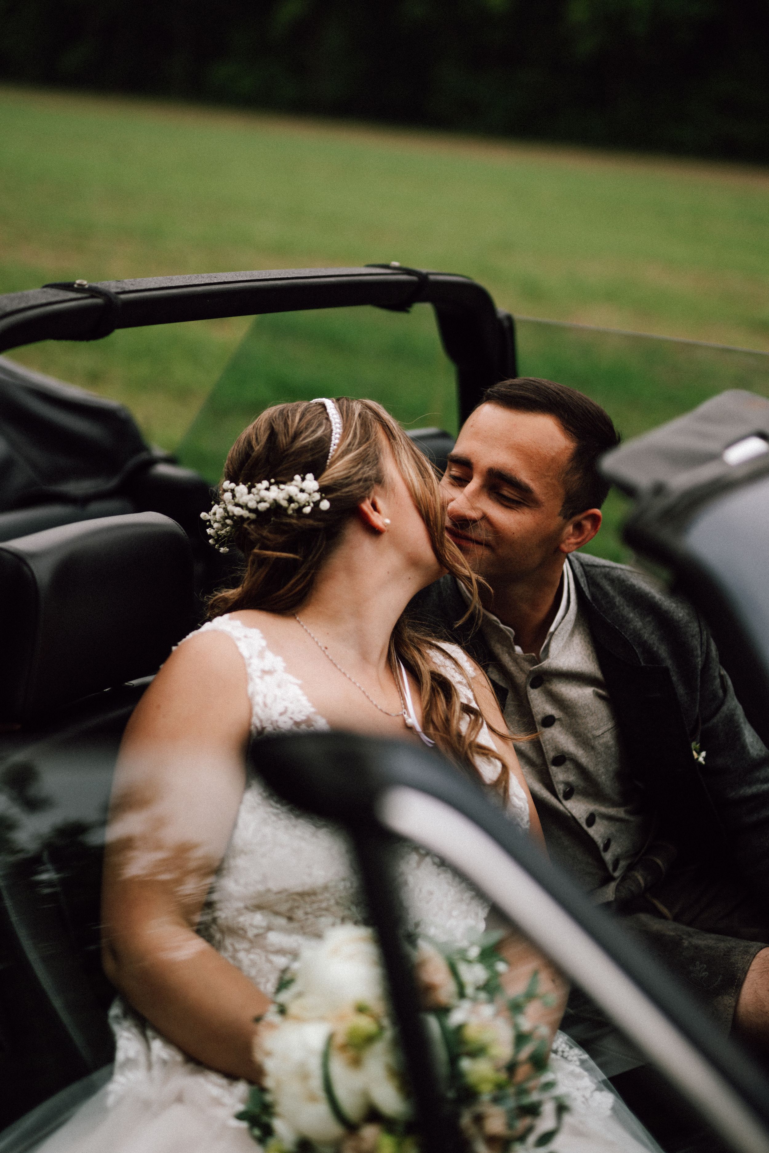 Romantic wedding photo taken through a car window showing the couple's intimate moment.