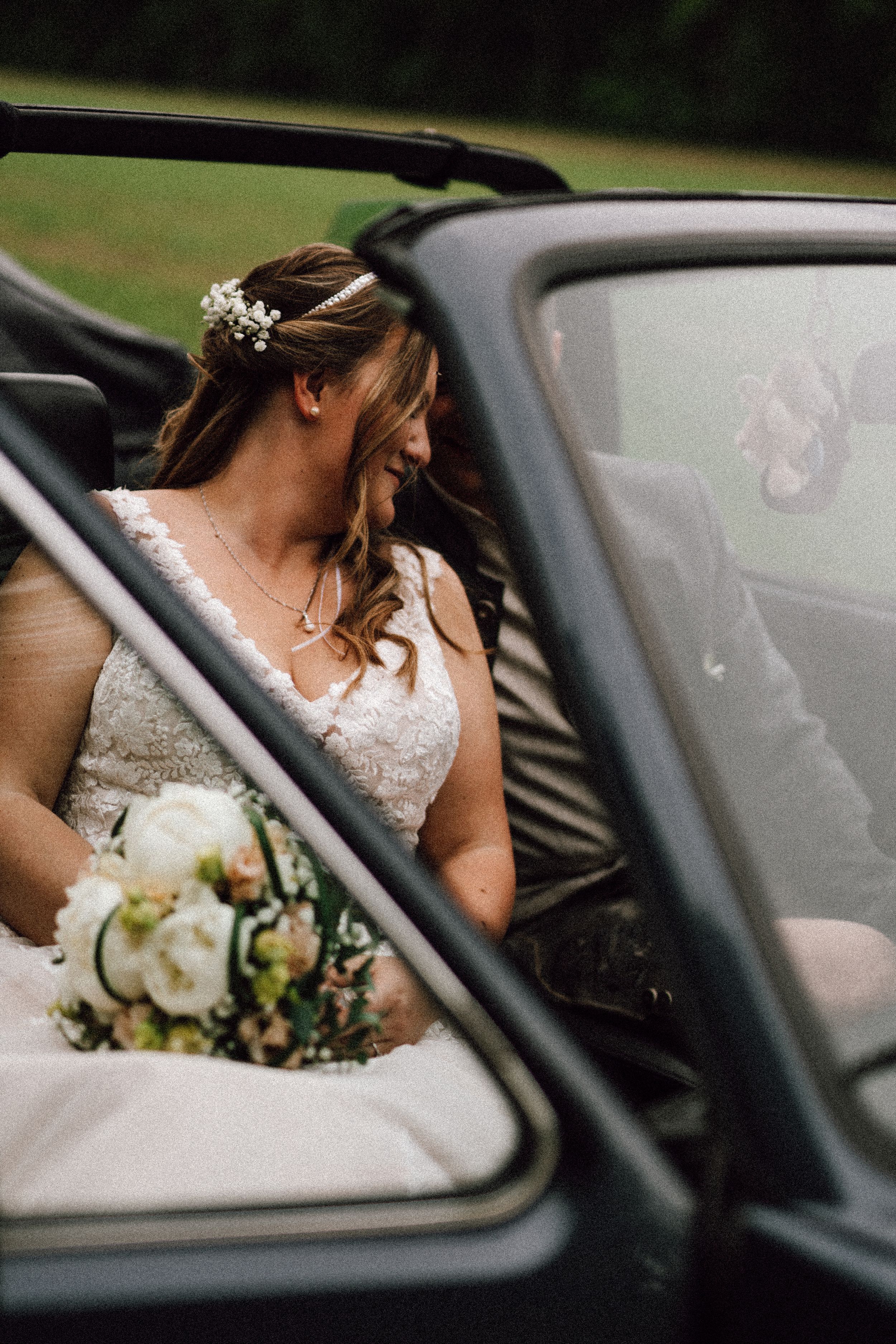 Wedding couple photographed through the window of a vintage car with bouquet visible.