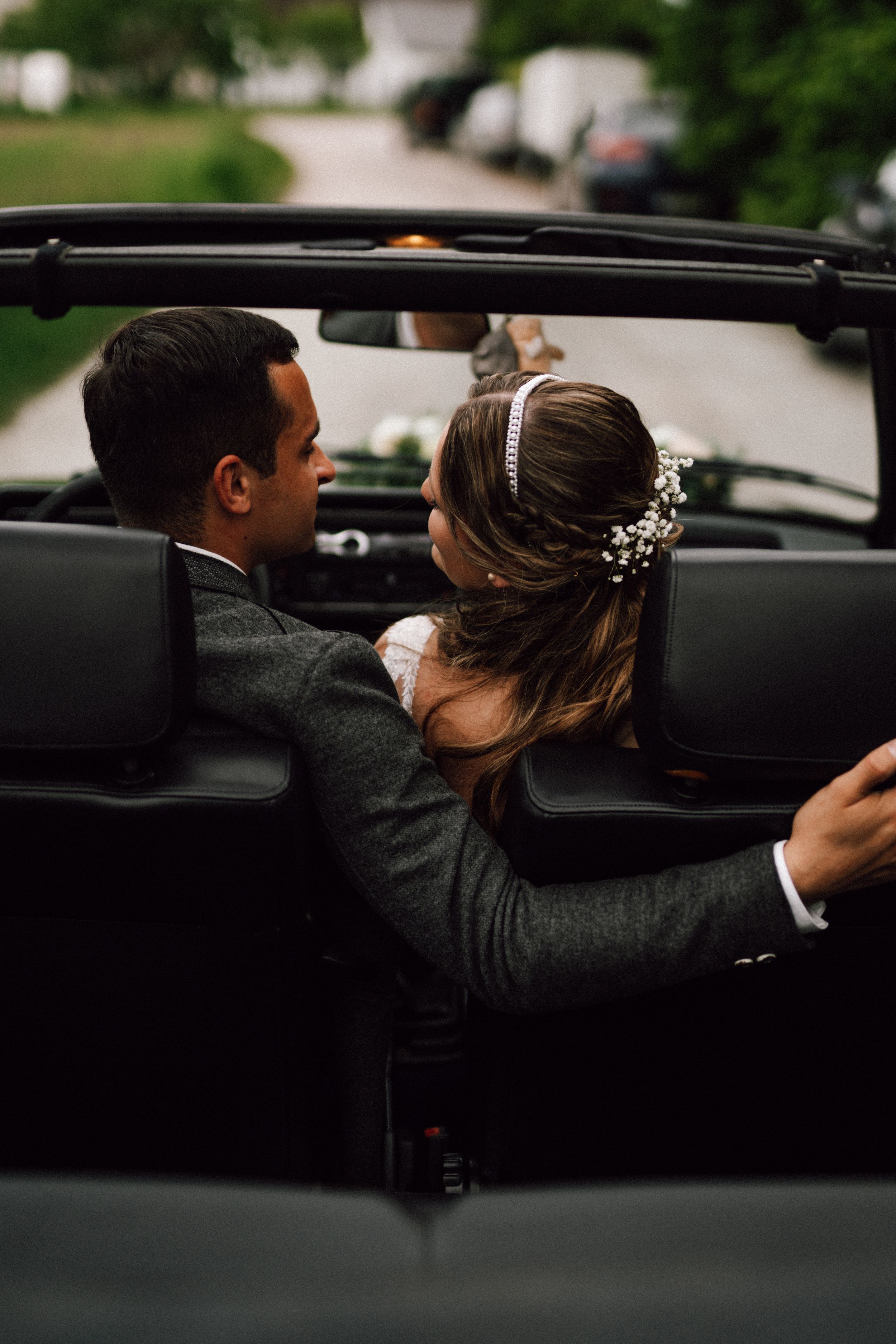 A romantic moment captured through a car window showing a couple in wedding attire sharing an intimate kiss.