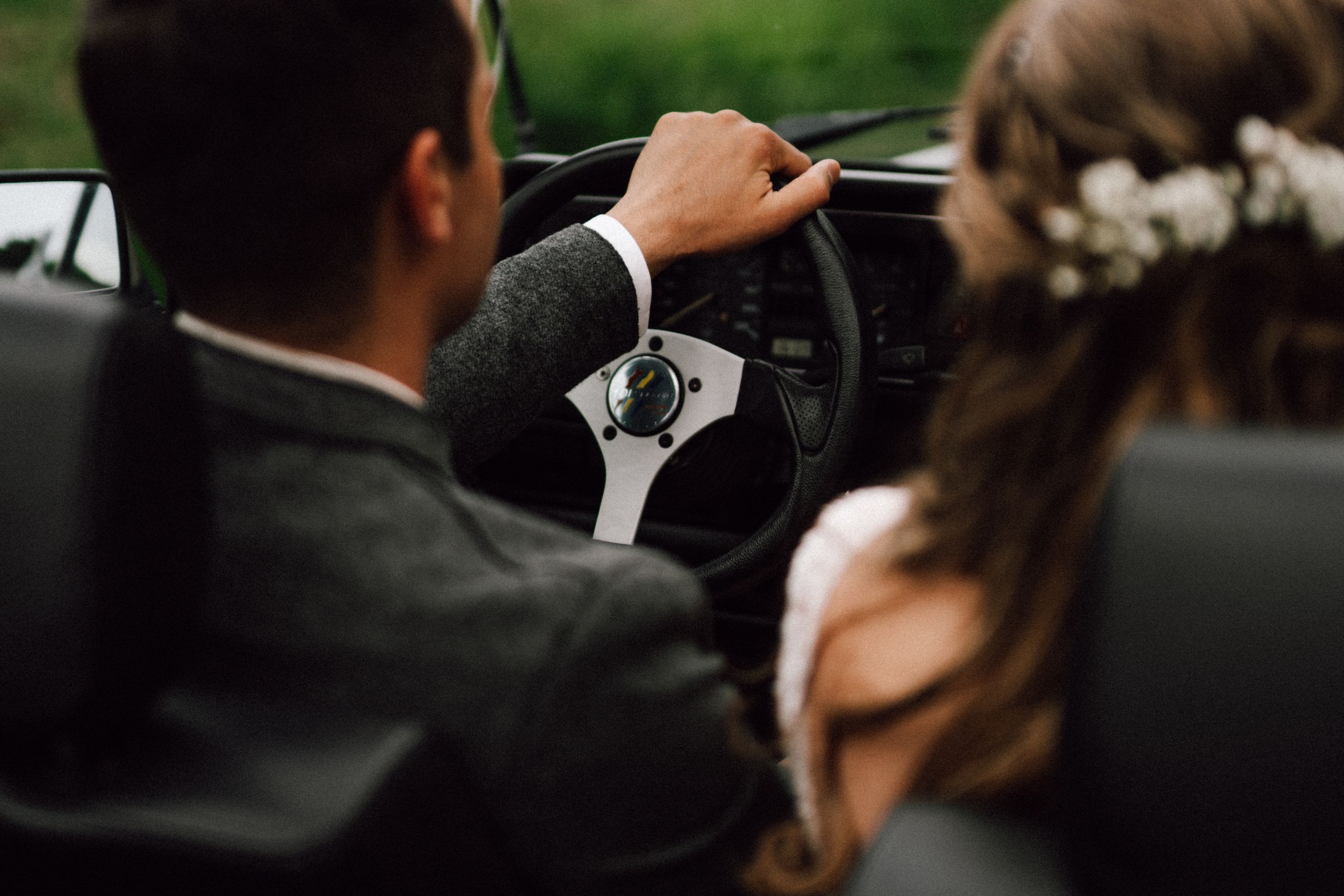Newlyweds share a tender moment through the window of a classic black car.