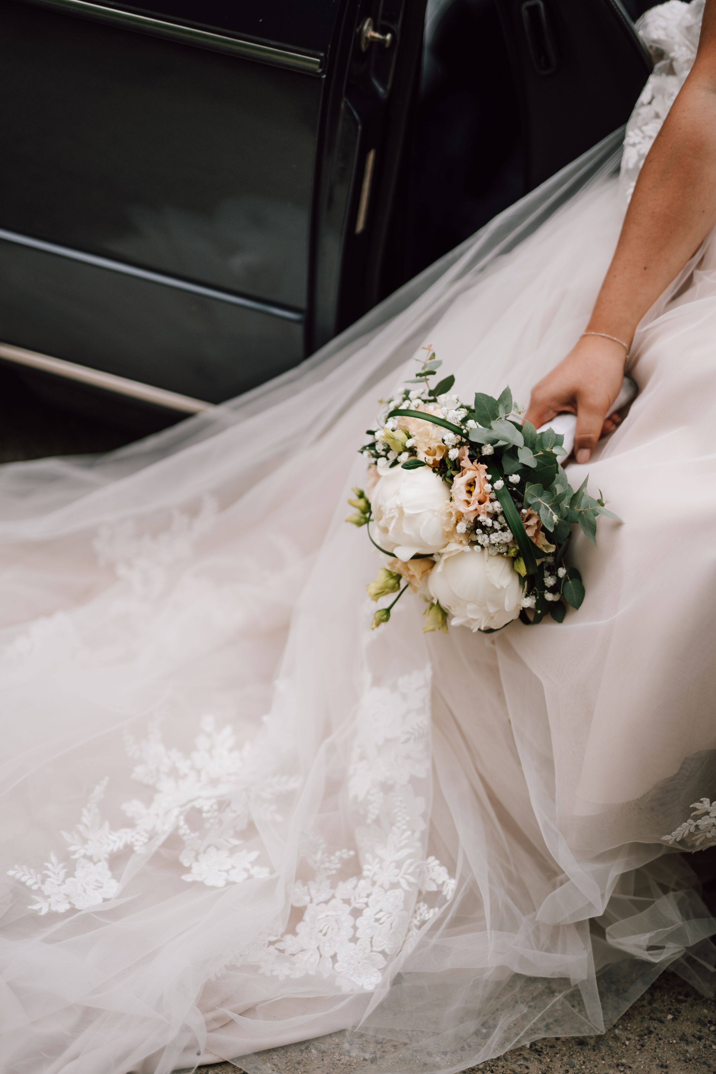 Close-up detail of a white wedding dress with lace appliques and floral bouquet.