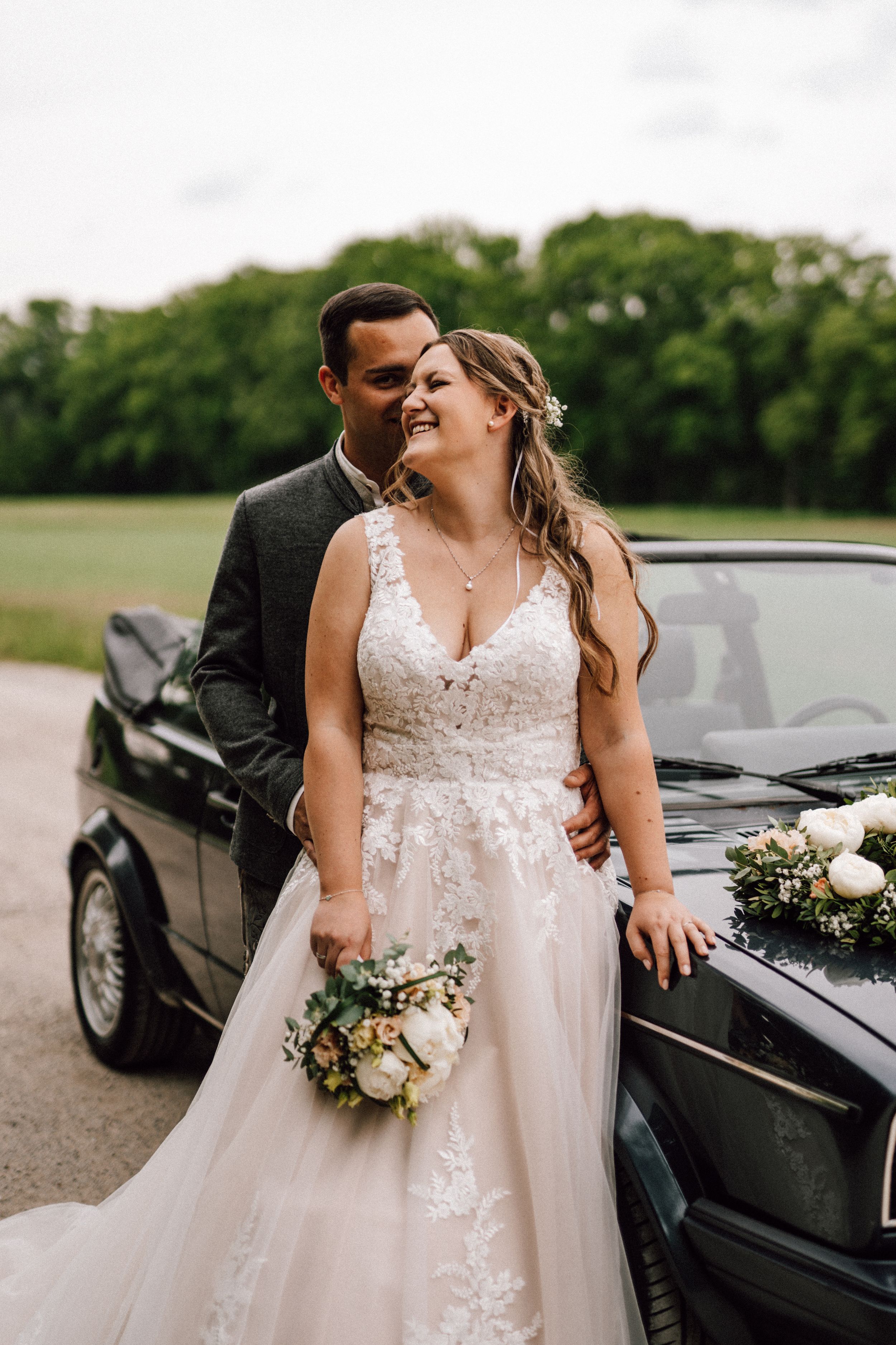 Romantic wedding photo by a classic black car with the bride holding a delicate bouquet.