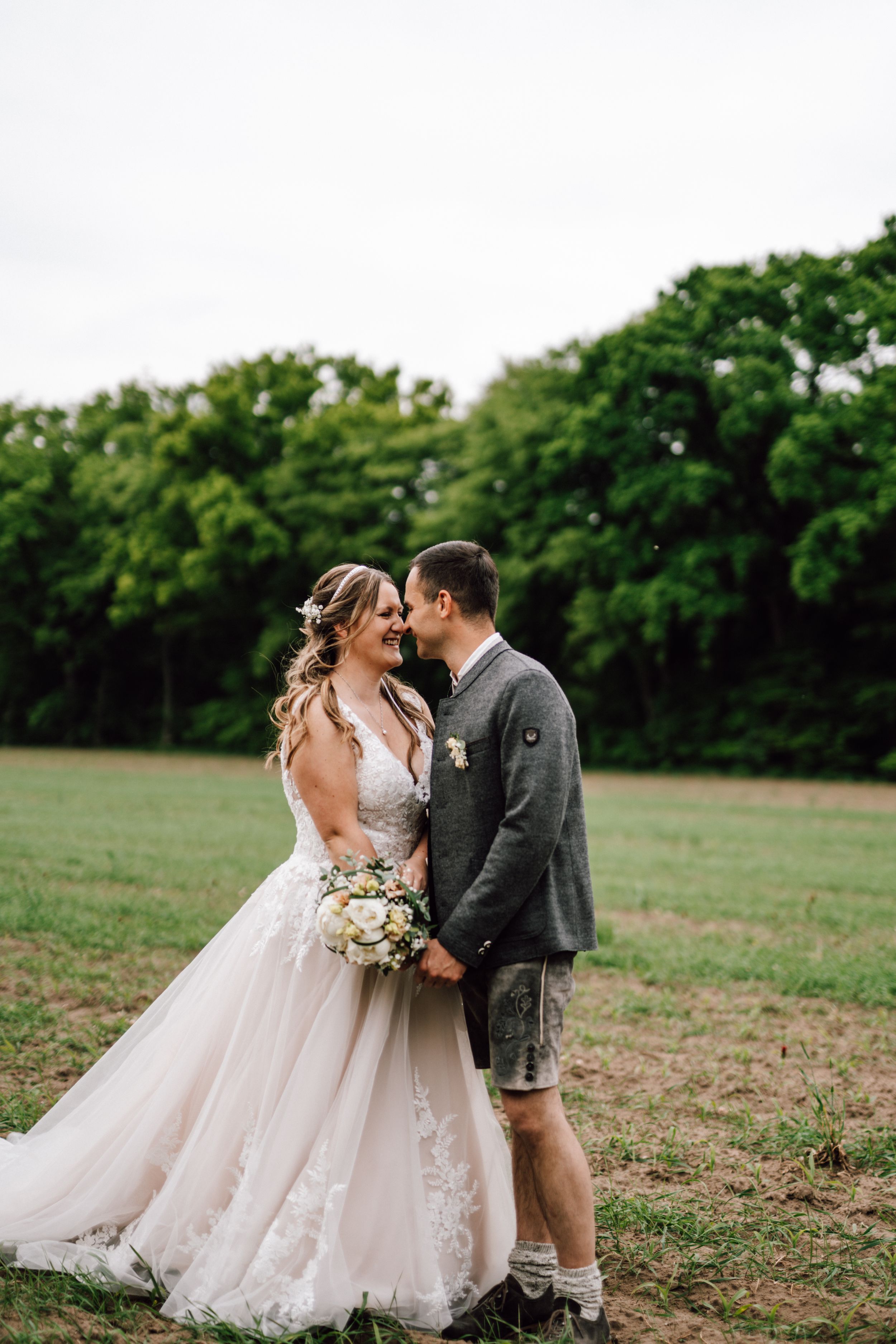 Couple shares an intimate moment in an open field with trees in the background.