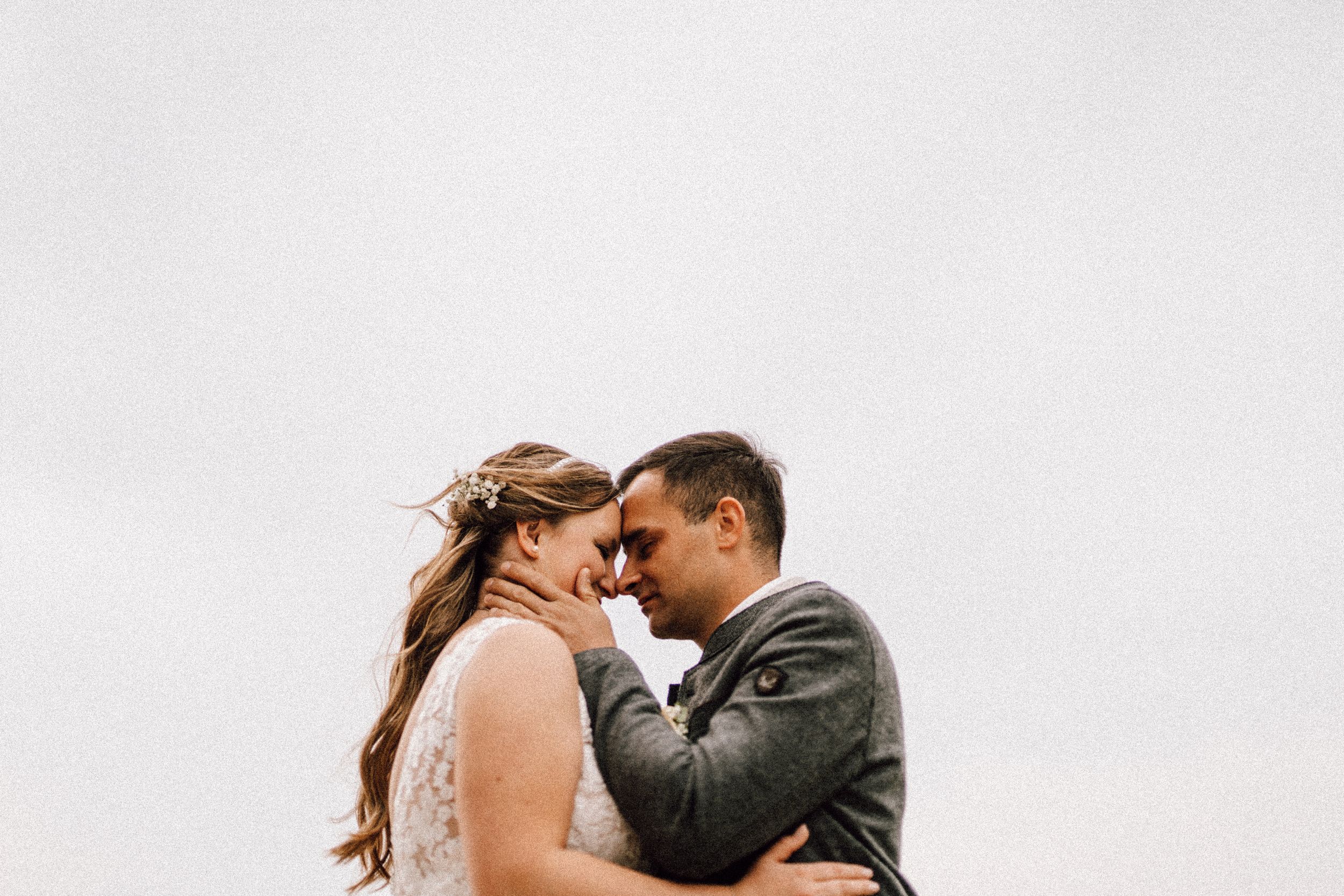 A romantic wedding couple sharing an intimate moment against an overcast sky.