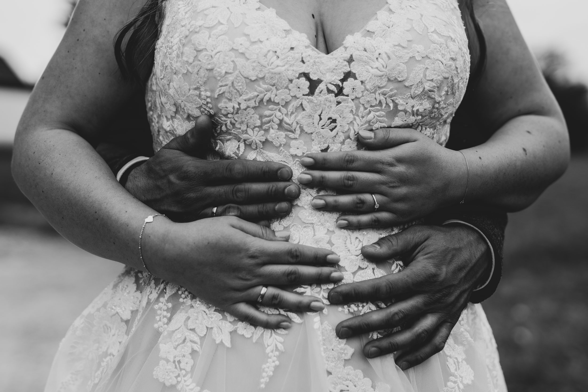 Black and white close-up of hands embracing around a lace wedding dress.