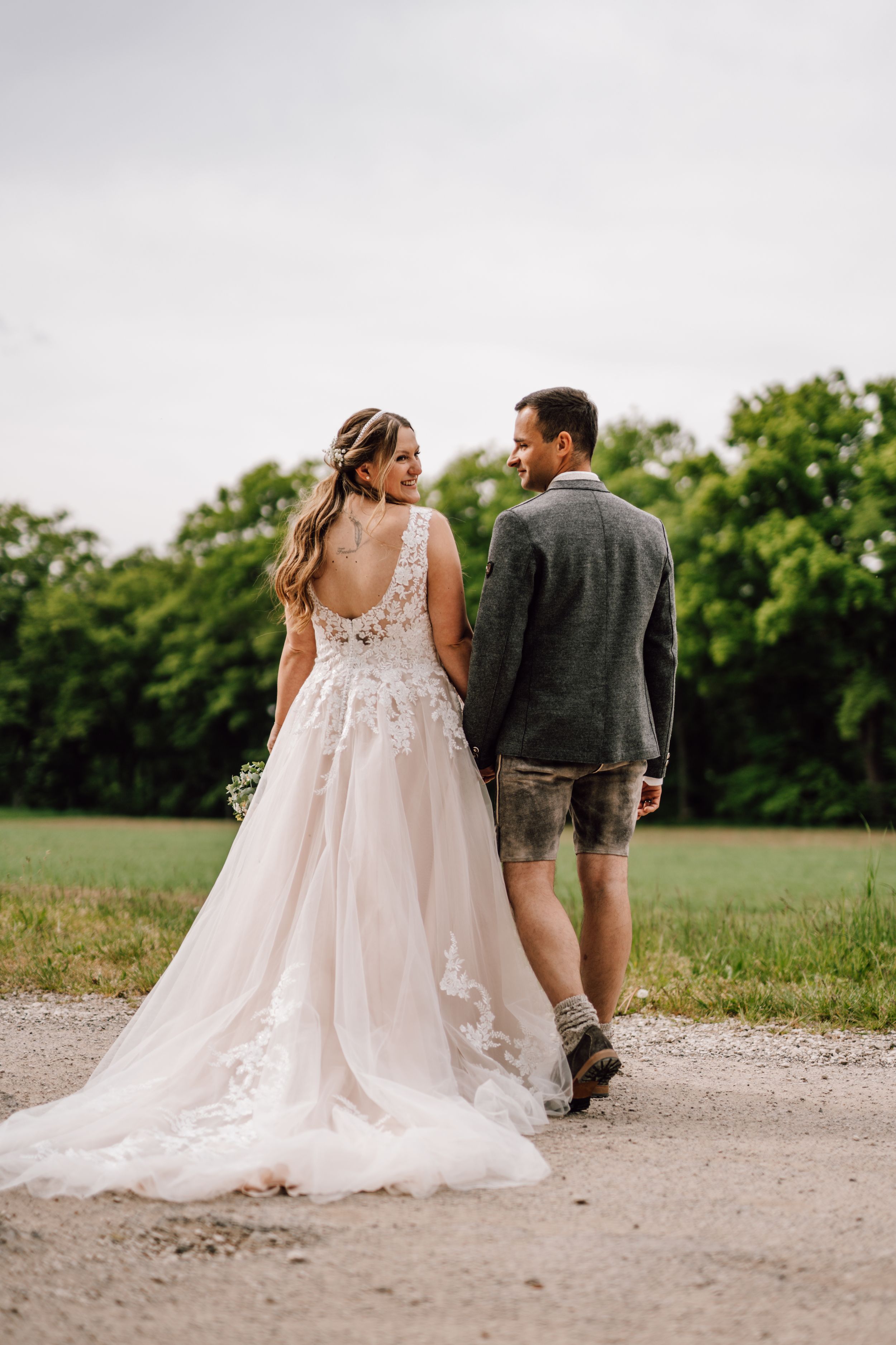 Newlyweds walking along a dirt path with the bride wearing a flowing lace gown.