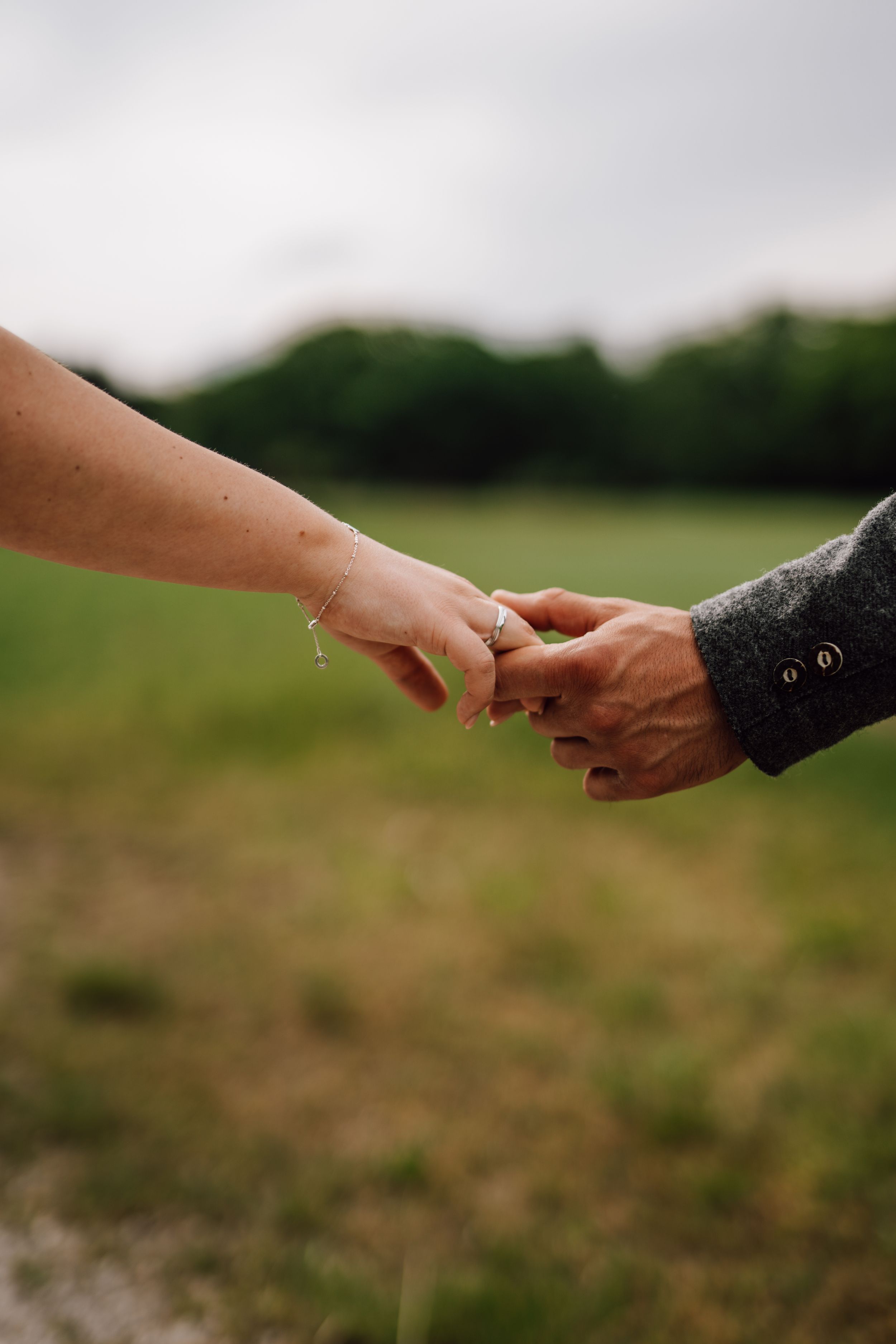 Close-up shot of hands holding with wedding rings in a natural outdoor setting.