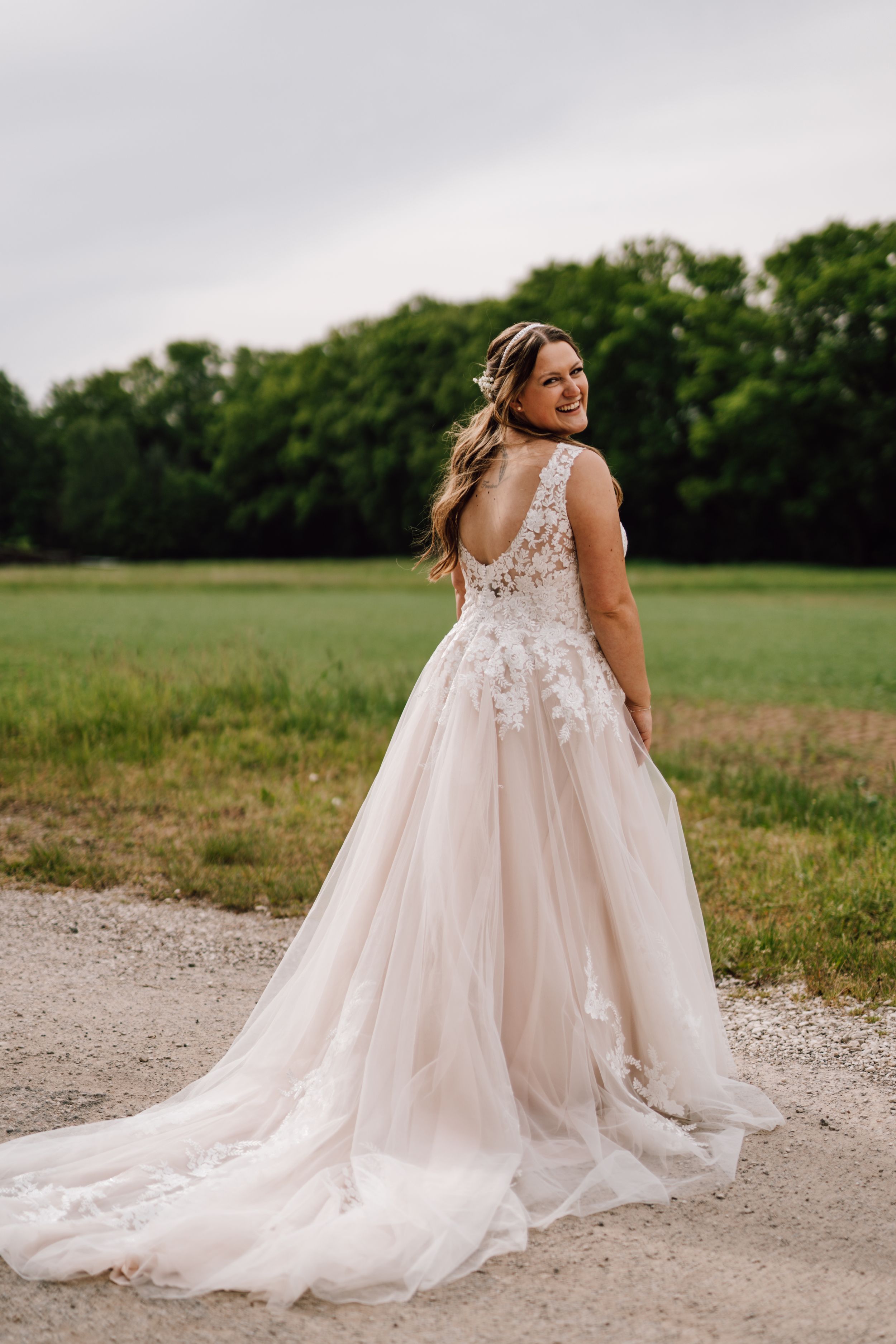Bride in a flowing lace wedding dress poses on a country path.