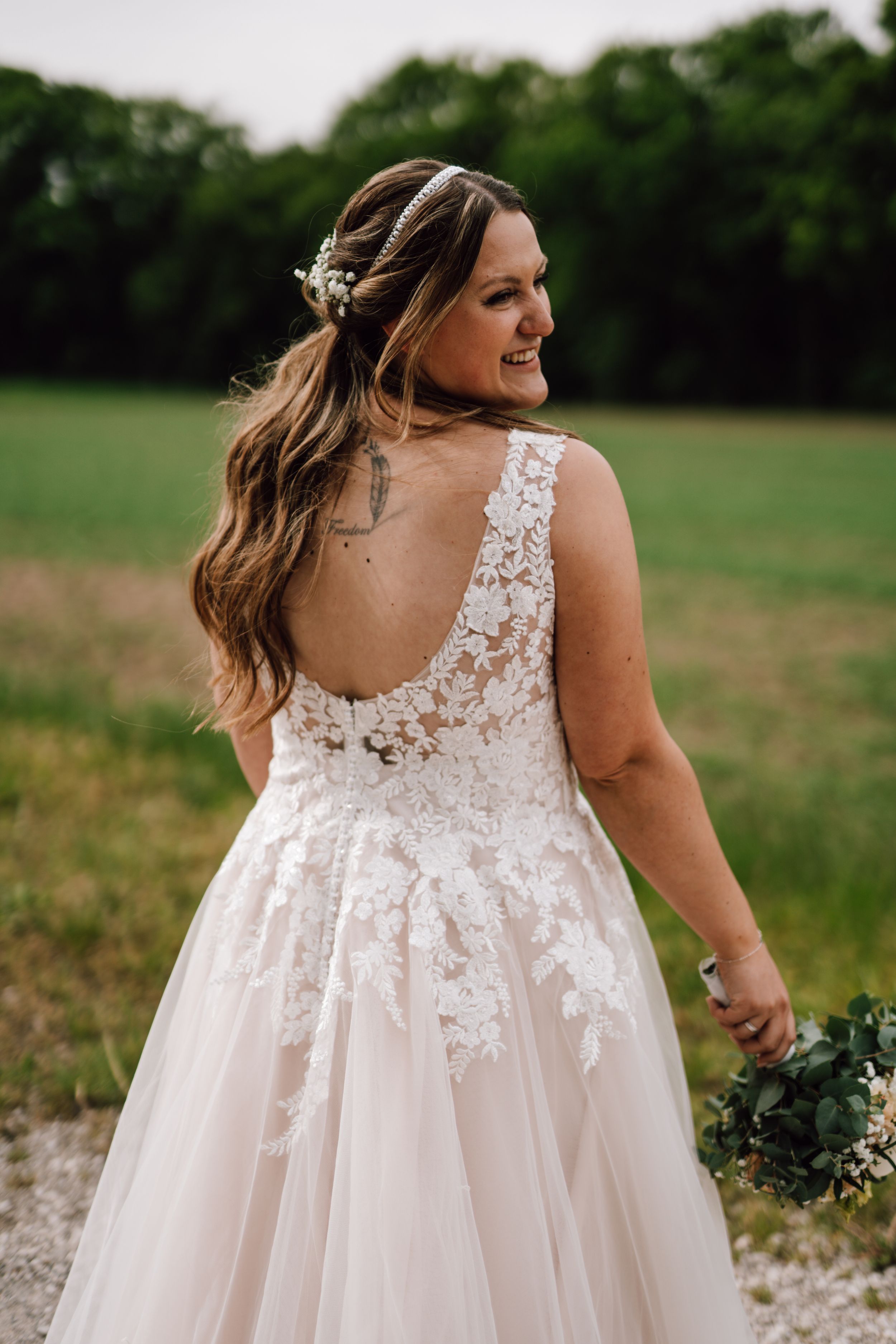 Bride in lace wedding dress with floral details poses in an outdoor setting.