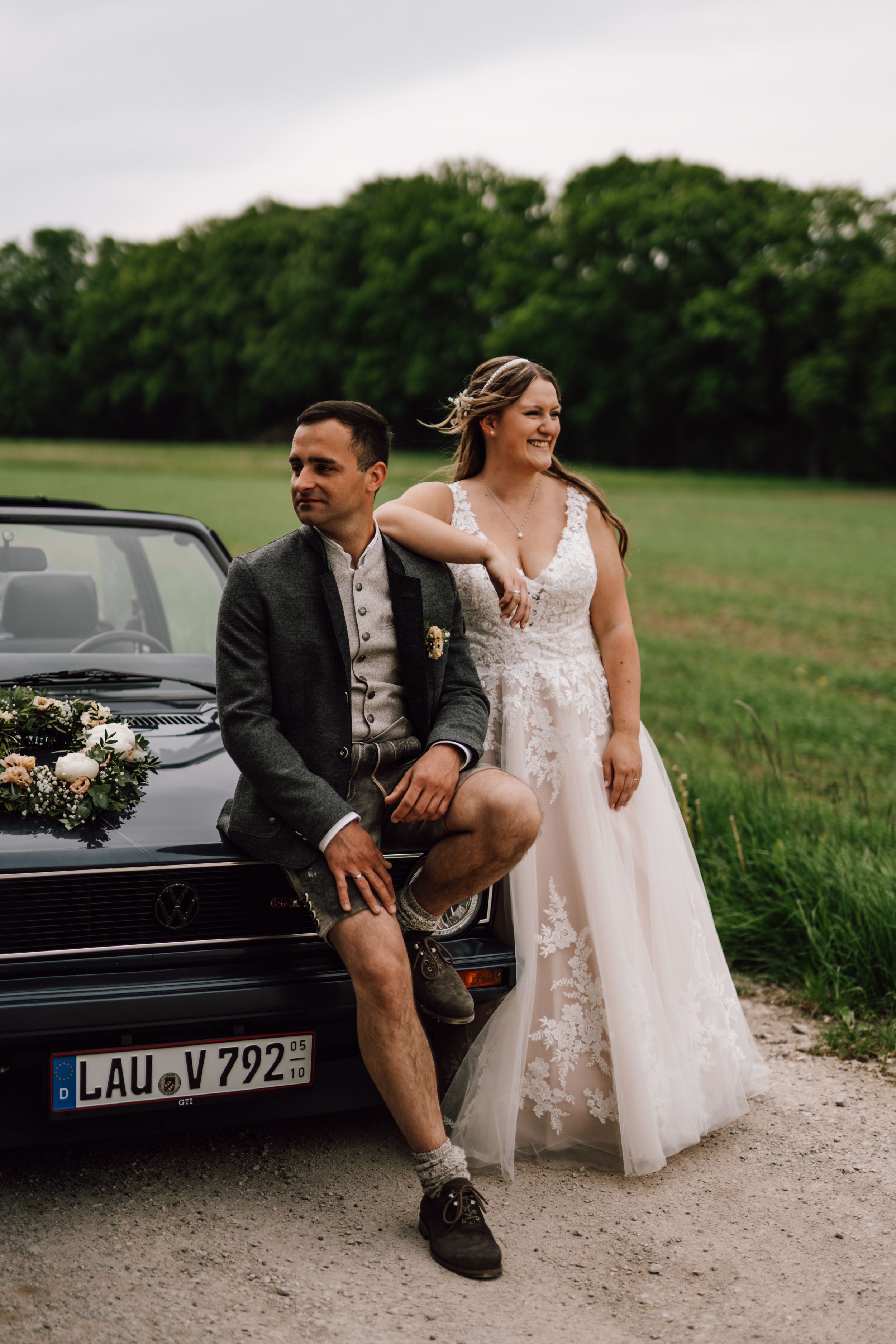 Wedding couple posing with vintage black convertible car in countryside setting.