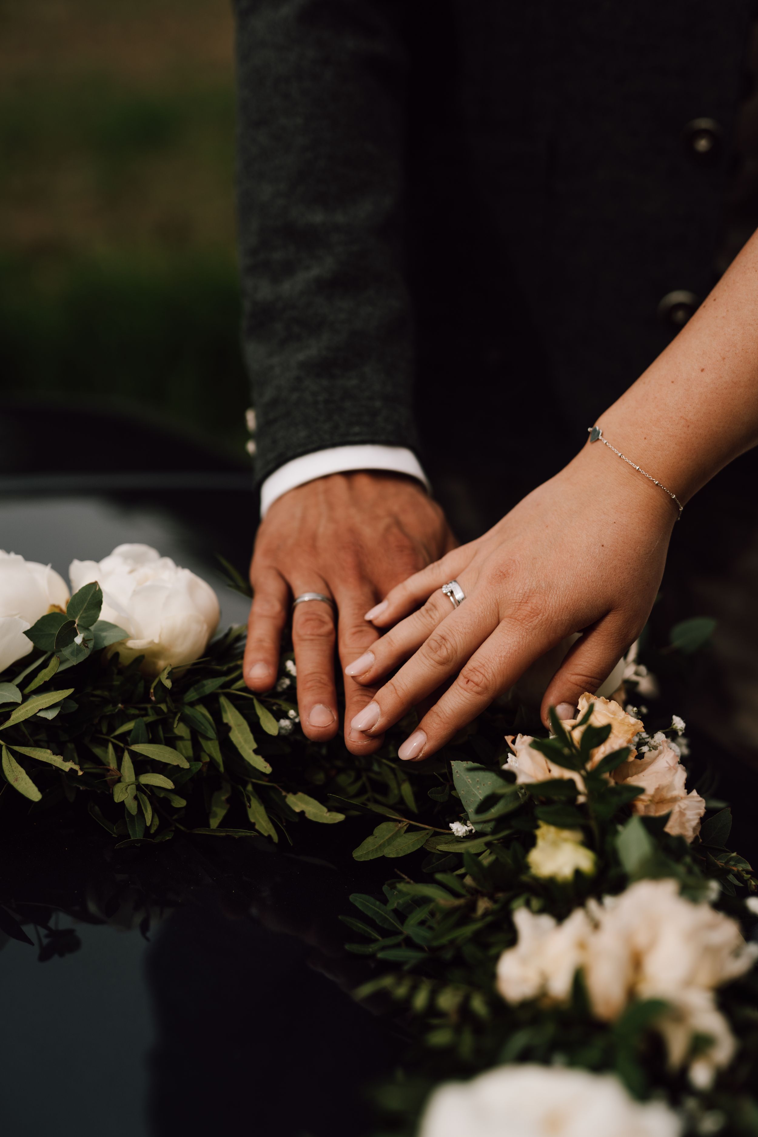 Close-up of wedding rings and hands resting on floral car decoration.