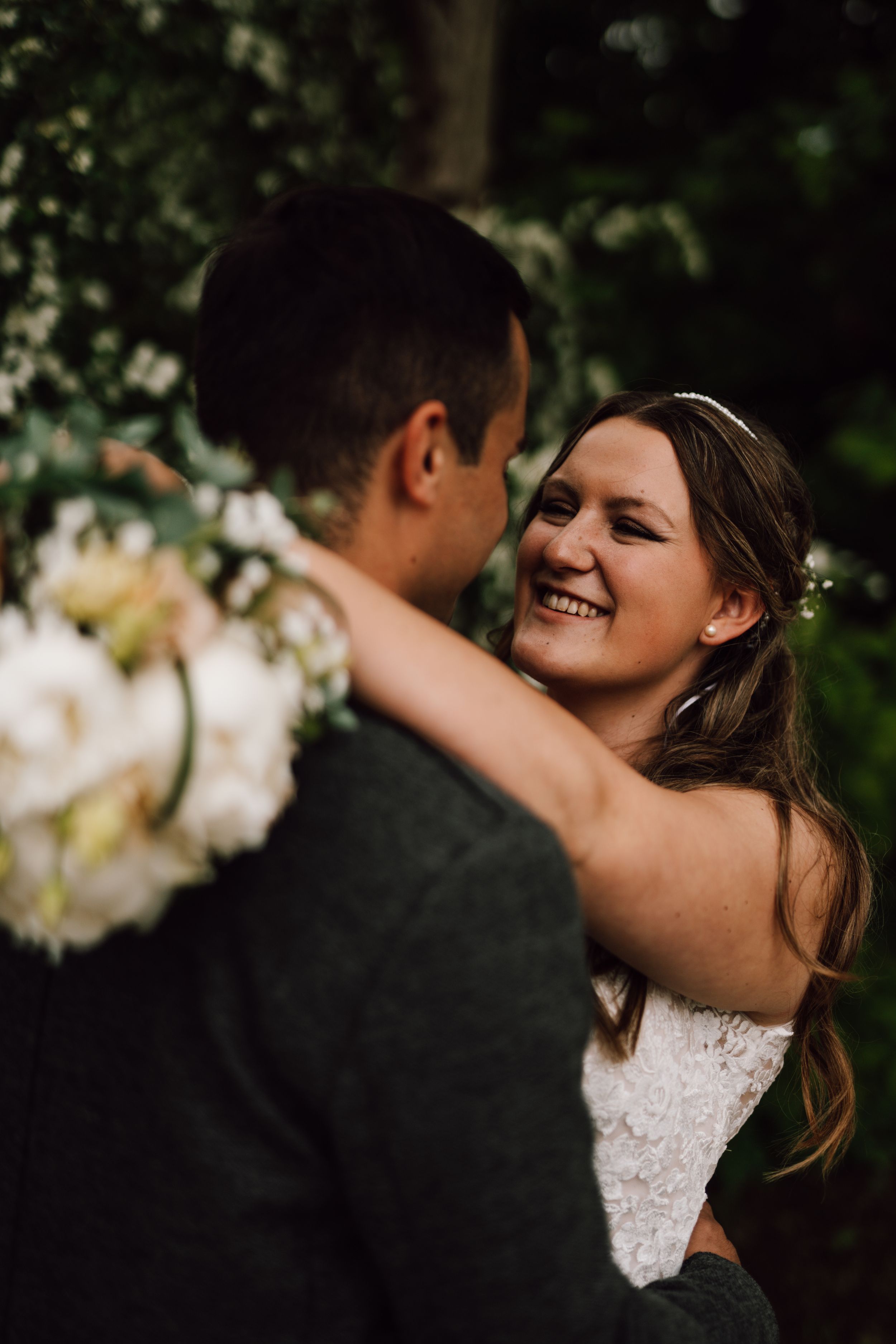 A romantic wedding moment captured in a garden setting with white flowers and greenery in the background.