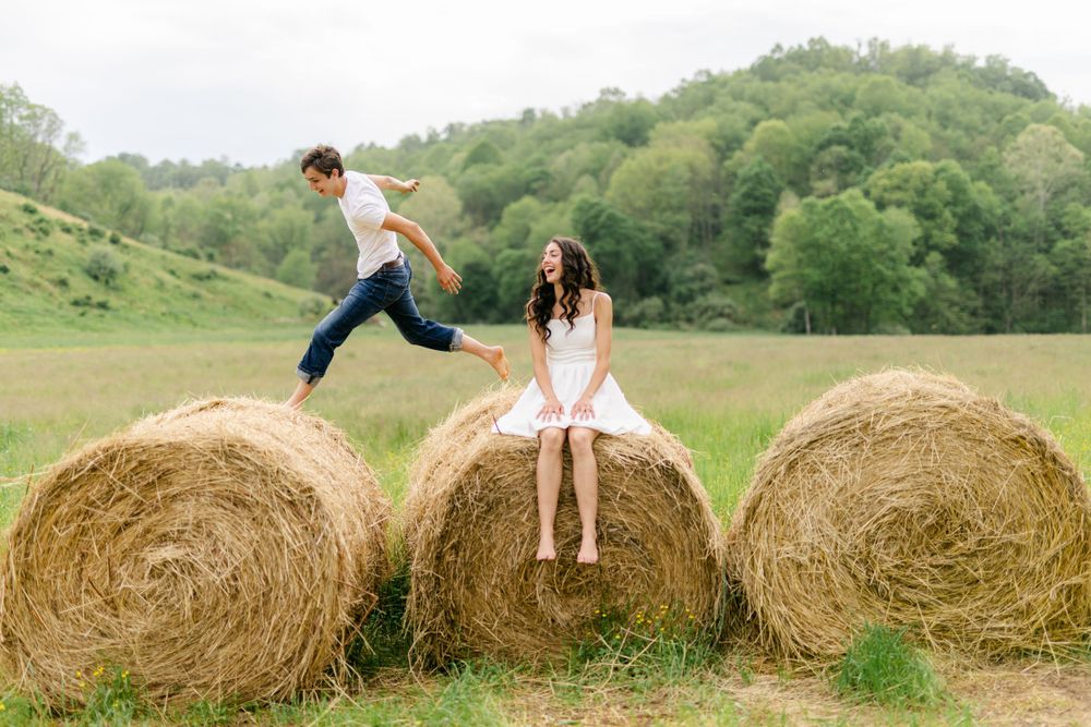 A man leaps across hay bales toward a woman sitting in a field.
