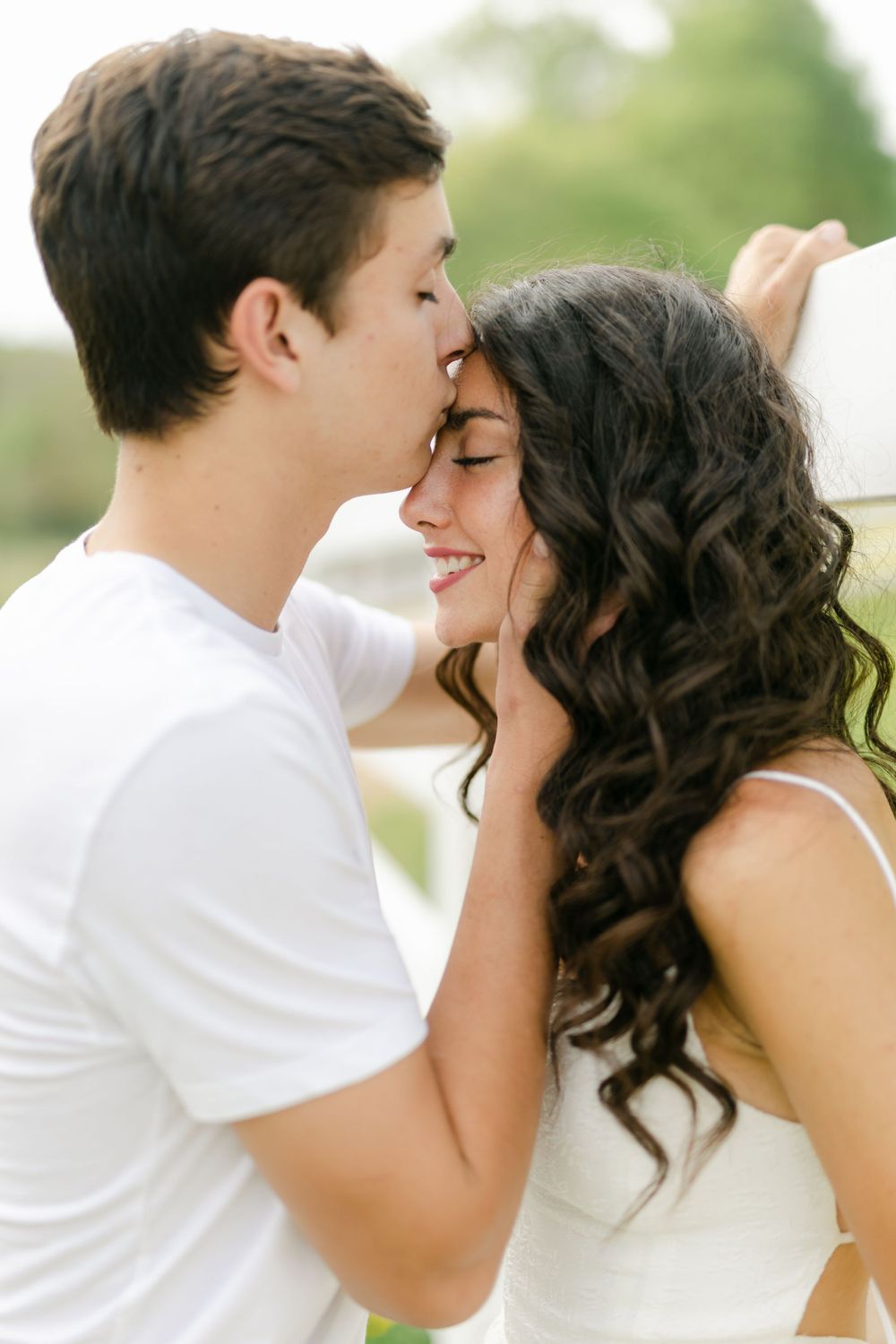 Young couple sharing a tender forehead kiss outdoors, man gently holding womans face.