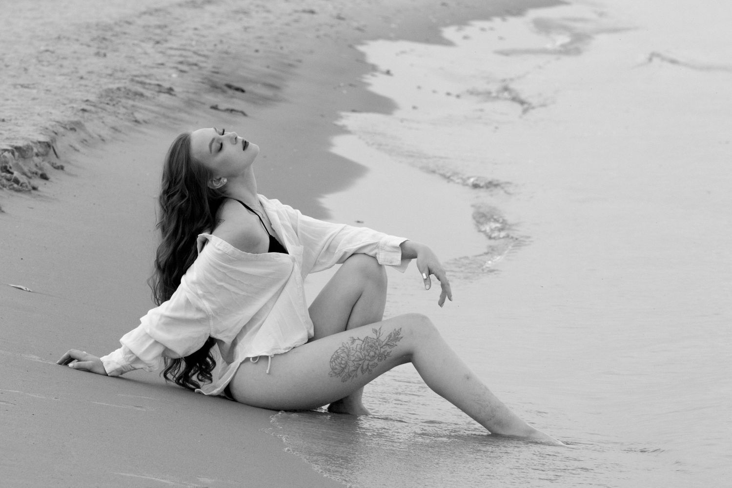 An artistic image of a woman with her feet in the water, sitting with her face towards the sky.