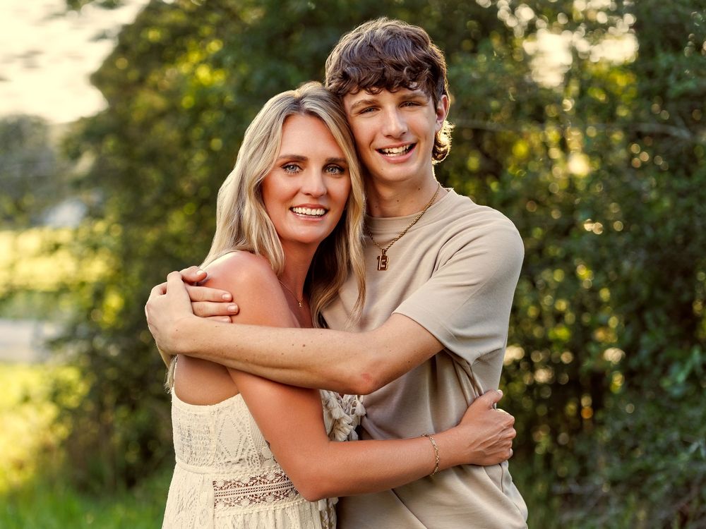 A smiling young couple embracing outdoors with lush green trees in the background during golden hour.