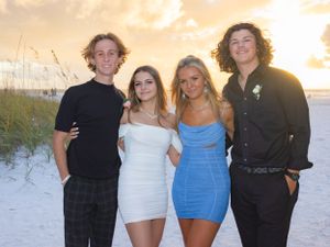 Four teenagers dressed up posing together on a sandy beach at golden sunset.