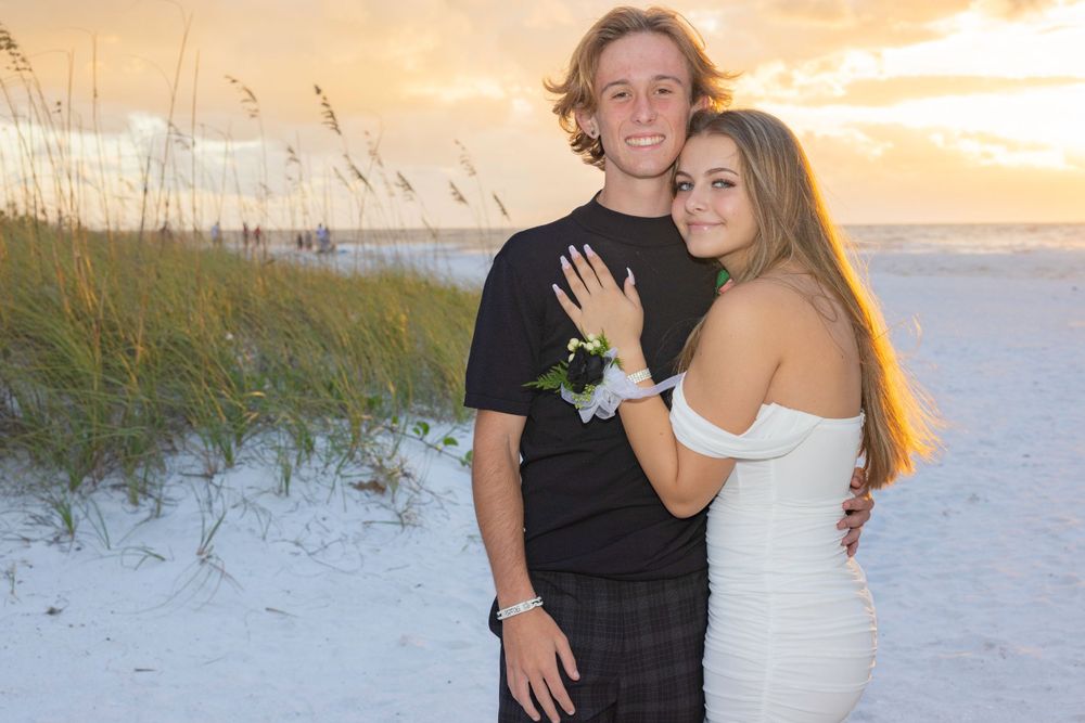 Young couple embracing on a white sand beach at sunset, woman showing engagement ring.