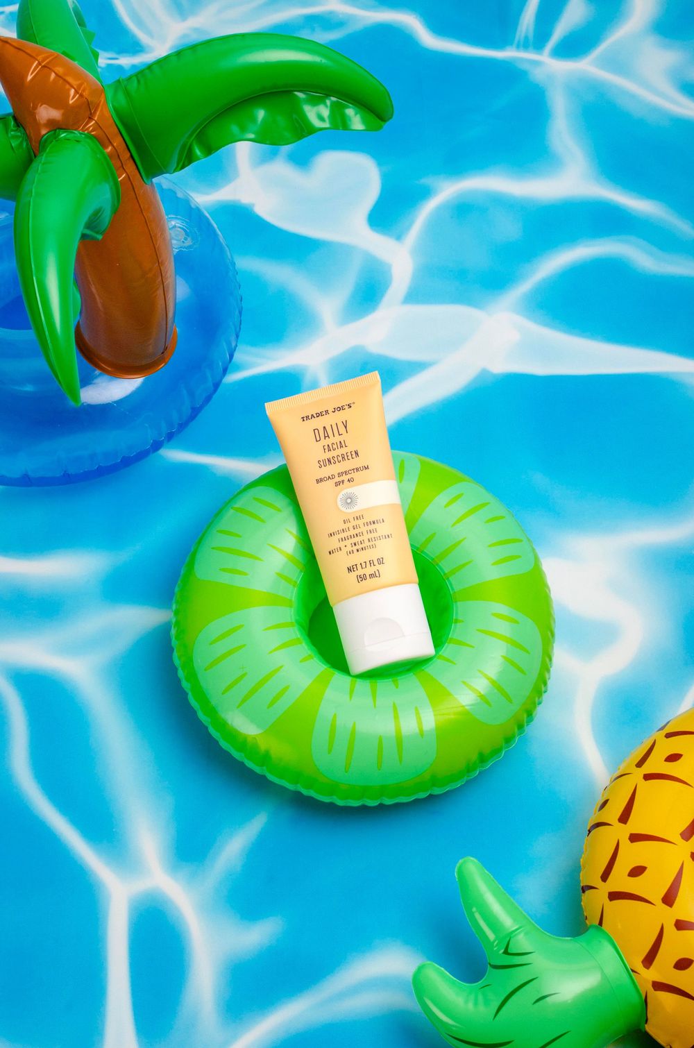 Trader Joe's Daily Facial Sunscreen tube resting on a green inflatable pool ring surrounded by tropical pool floats.