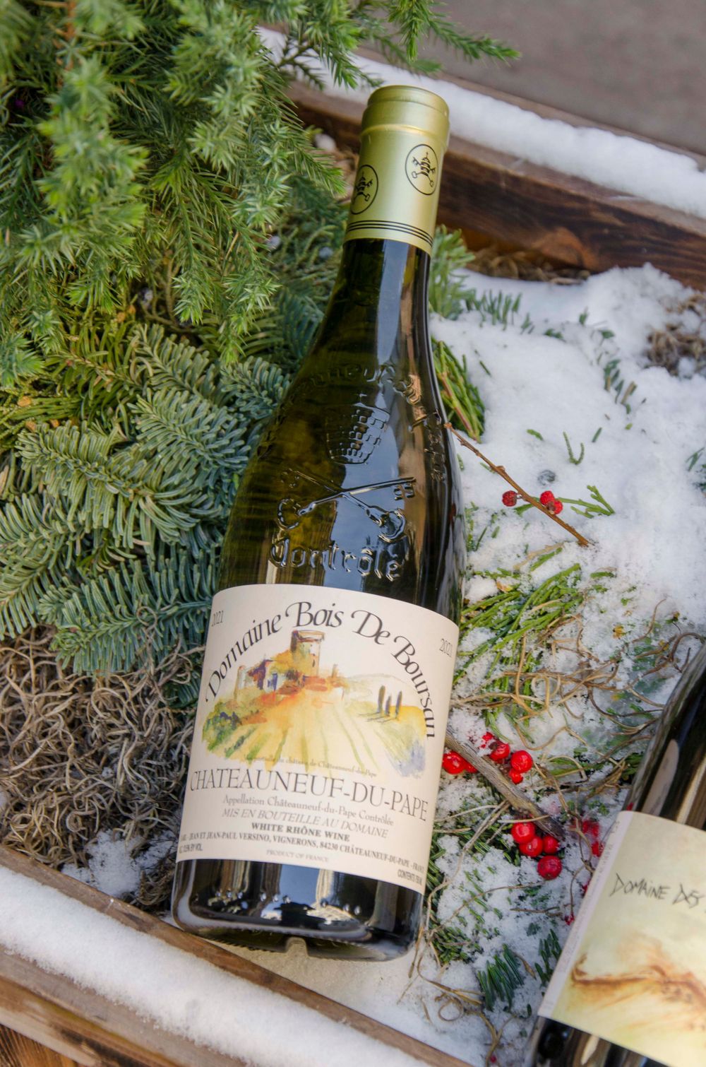 Wine bottle from Domaine Bos Dei Aires nestled in snow with evergreen branches.