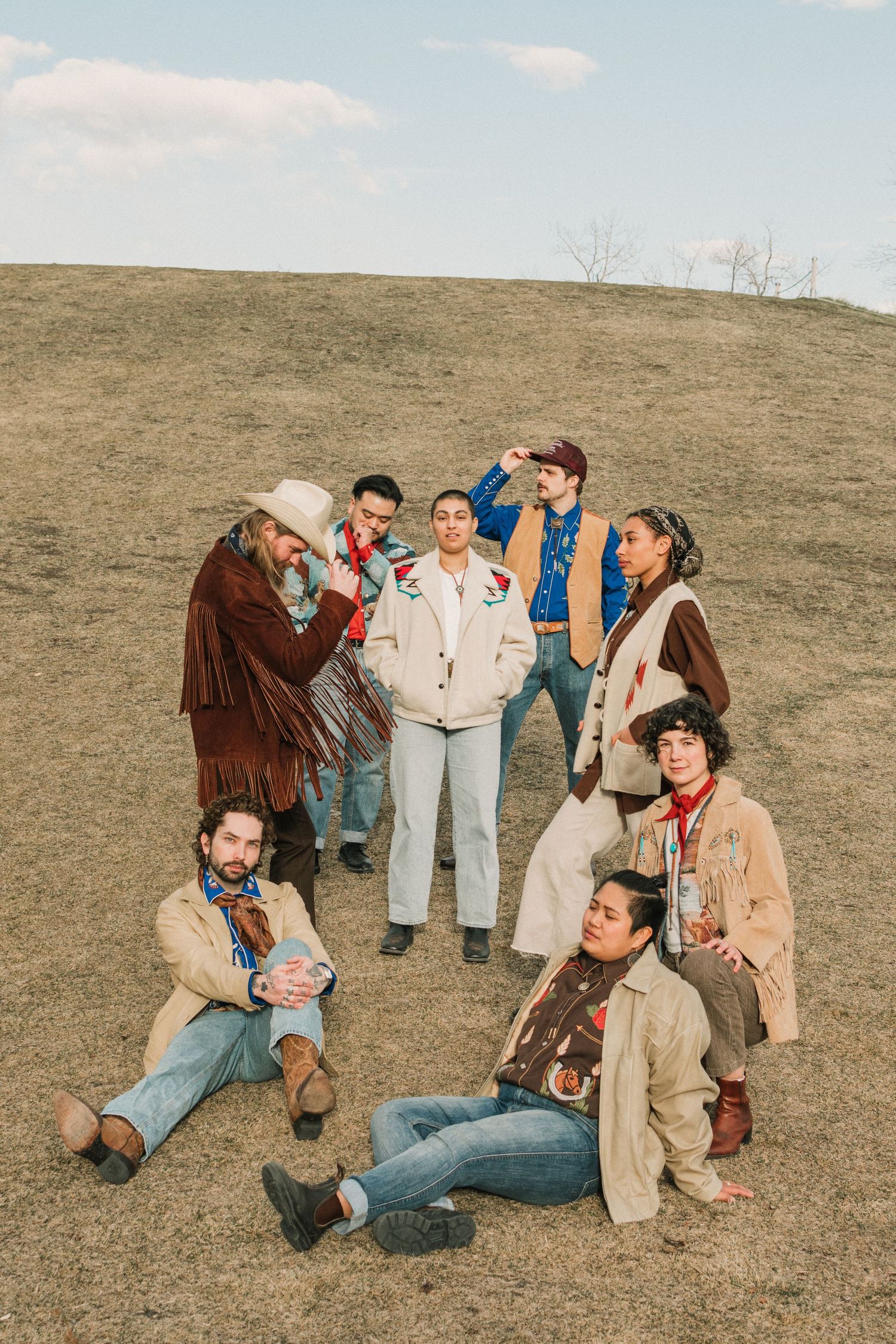 A casual group poses together on a brown hillside wearing vintage-inspired clothing and denim.
