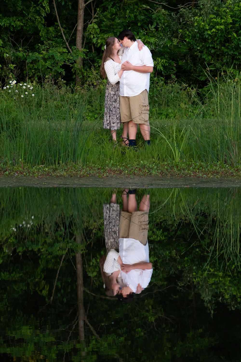 A couple's reflection perfectly mirrored in still water surrounded by lush greenery.