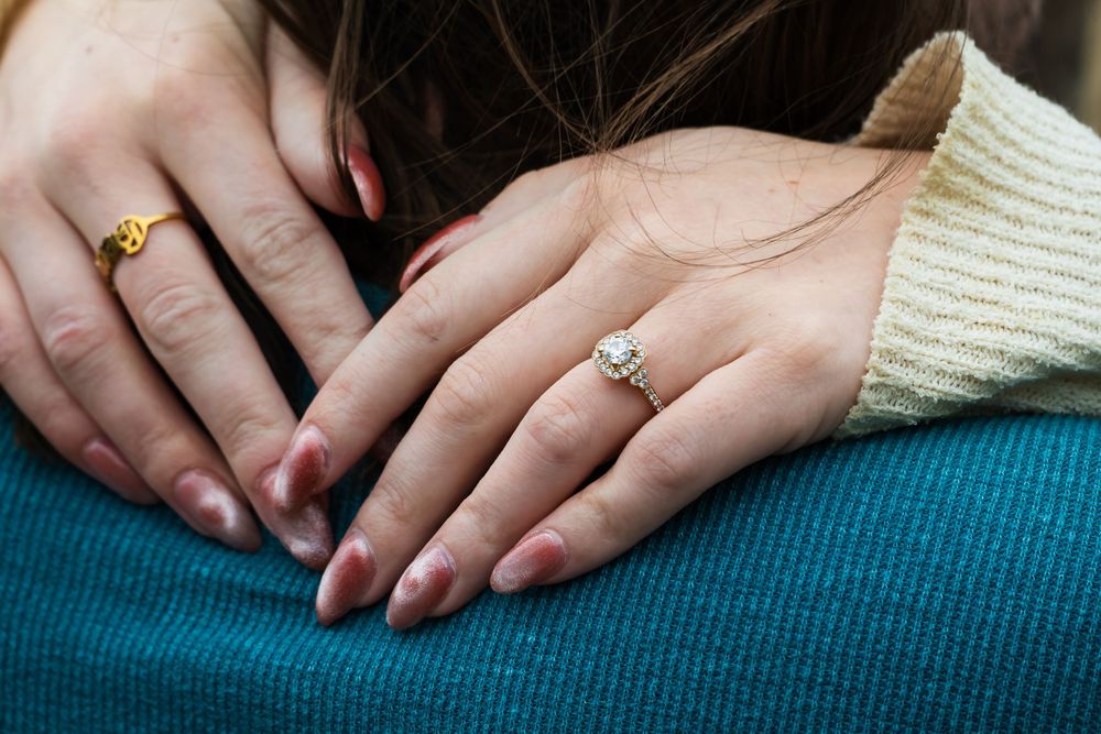 Close-up of hands wearing engagement ring resting on blue fabric.