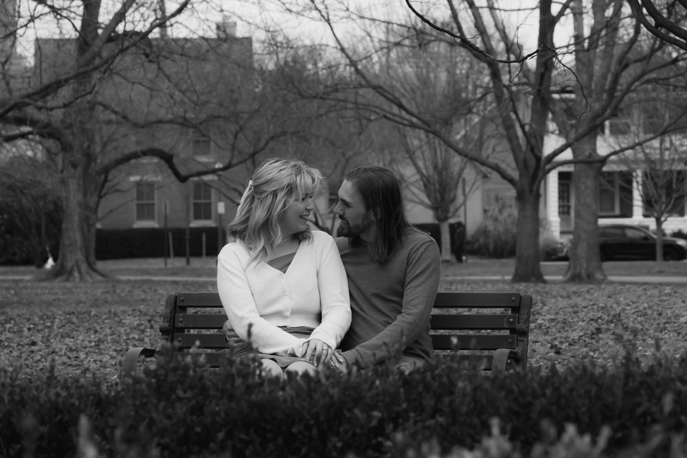 Black and white romantic portrait of couple sitting close together on a park bench.