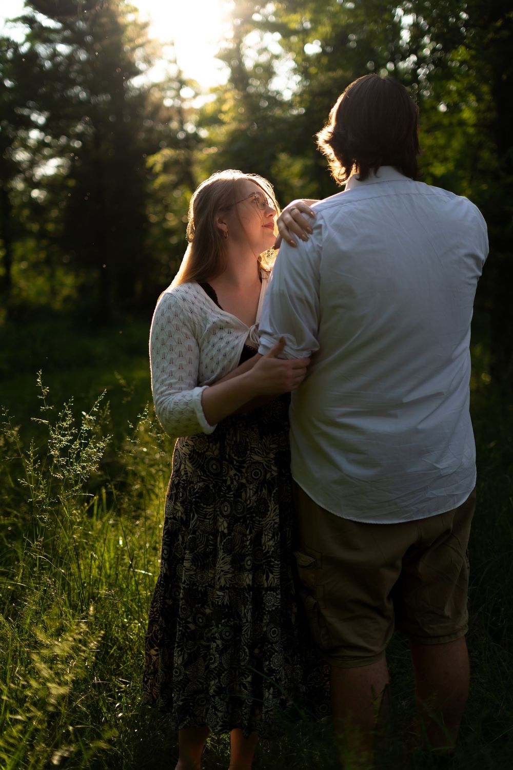 A couple shares a joyful moment in golden sunset light among tall grass.