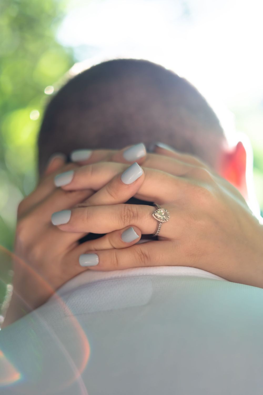 Hands with pale nail polish and an engagement ring rest gently in an intimate embrace.